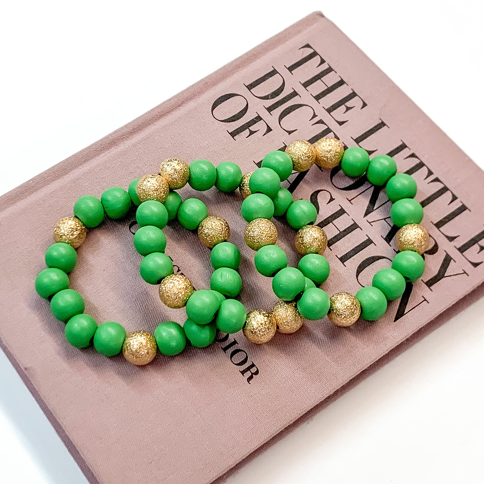 Pictured on a mauve colored book is a set of green beaded bracelets with gold beaded spacers. 