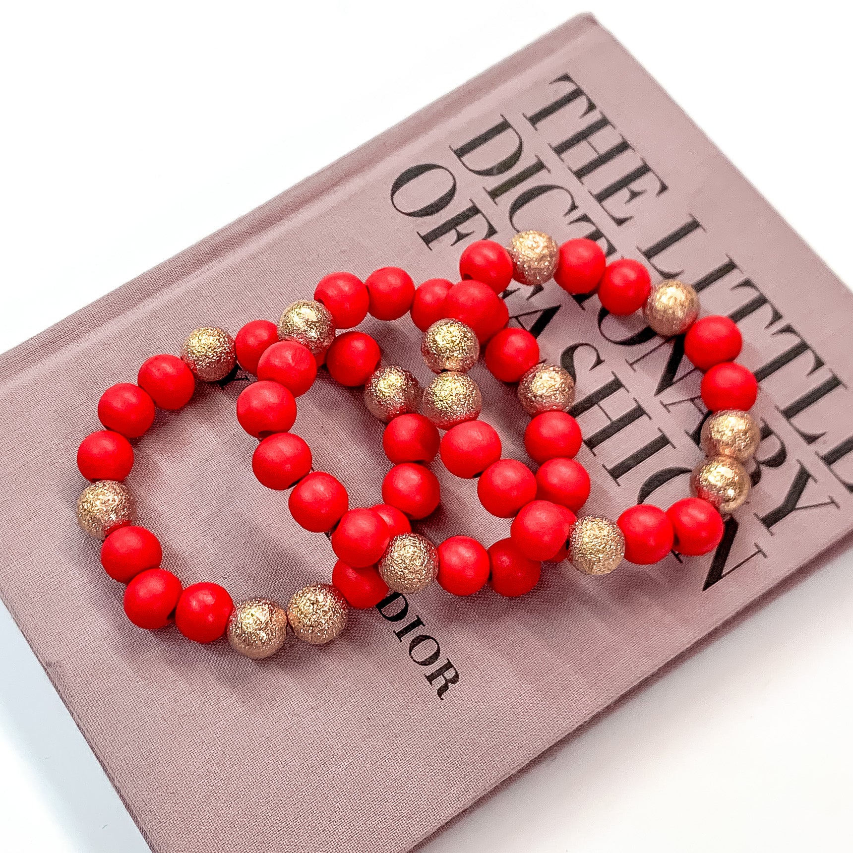 Pictured on a mauve colored book is a set of red beaded bracelets with gold beaded spacers. 