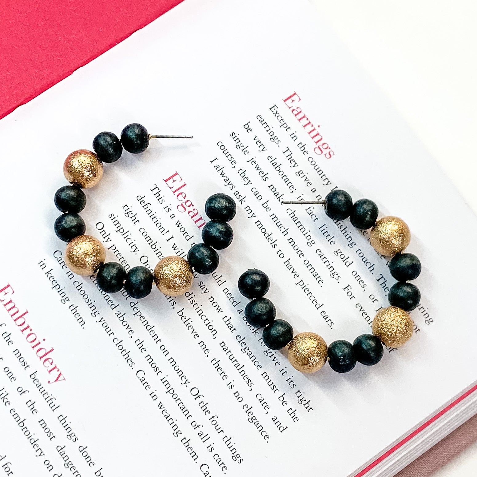 Pictured on an open book is a pair of black beaded hoop earrings with gold beaded spacers.