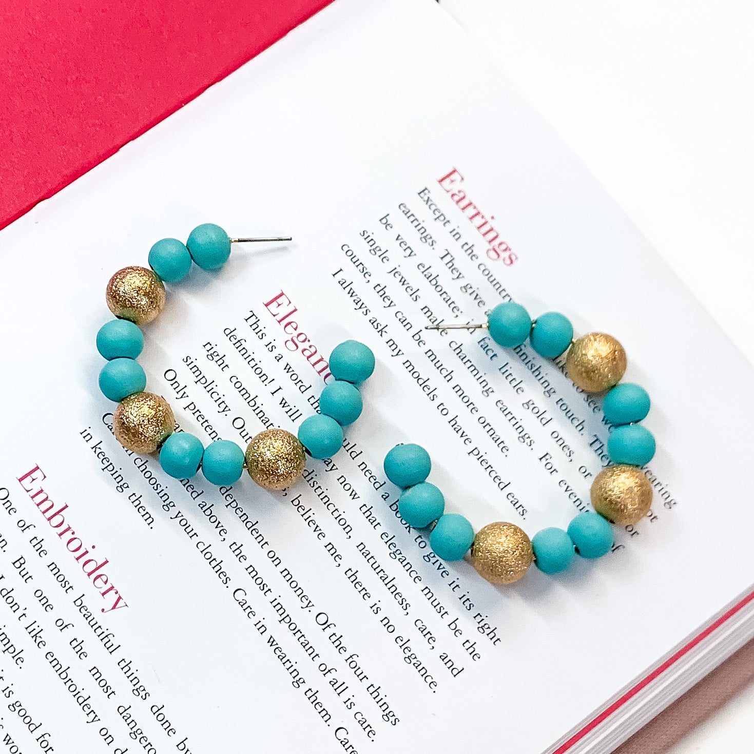 Pictured on an open book is a pair of sky blue beaded hoop earrings with gold beaded spacers. 