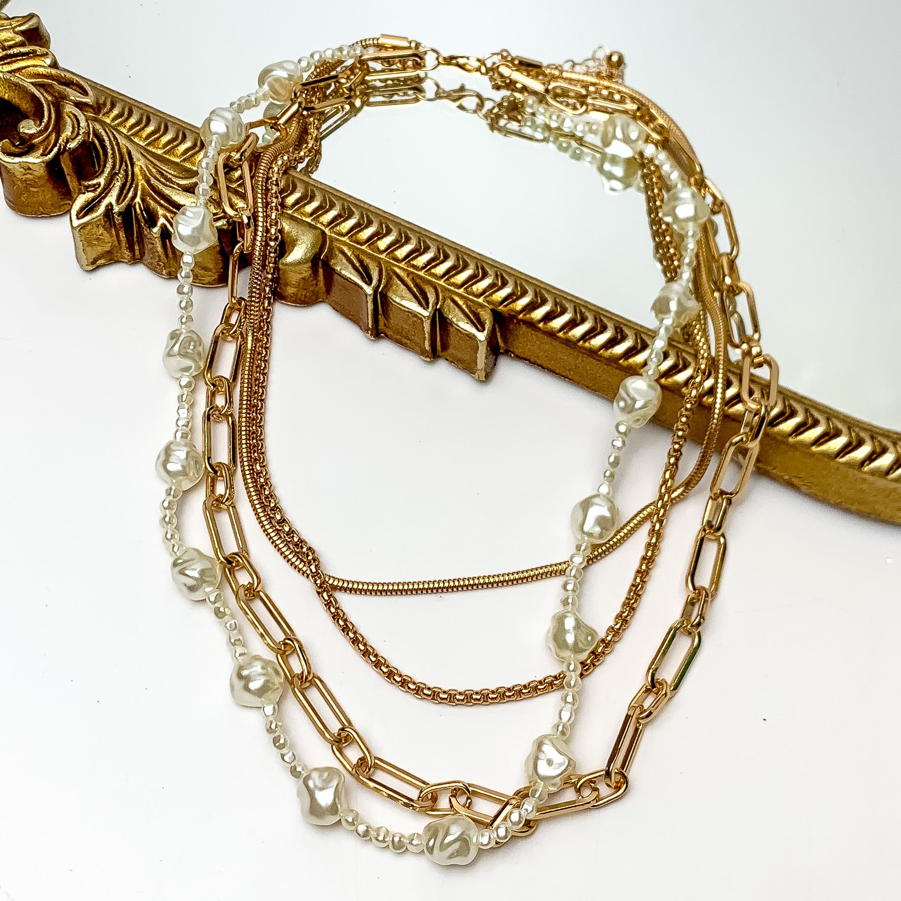 Four Strand Gold Tone Chain Necklace With Pearl Strand. Pictured on a white background with part of the necklace laying on a mirror with a gold trim.