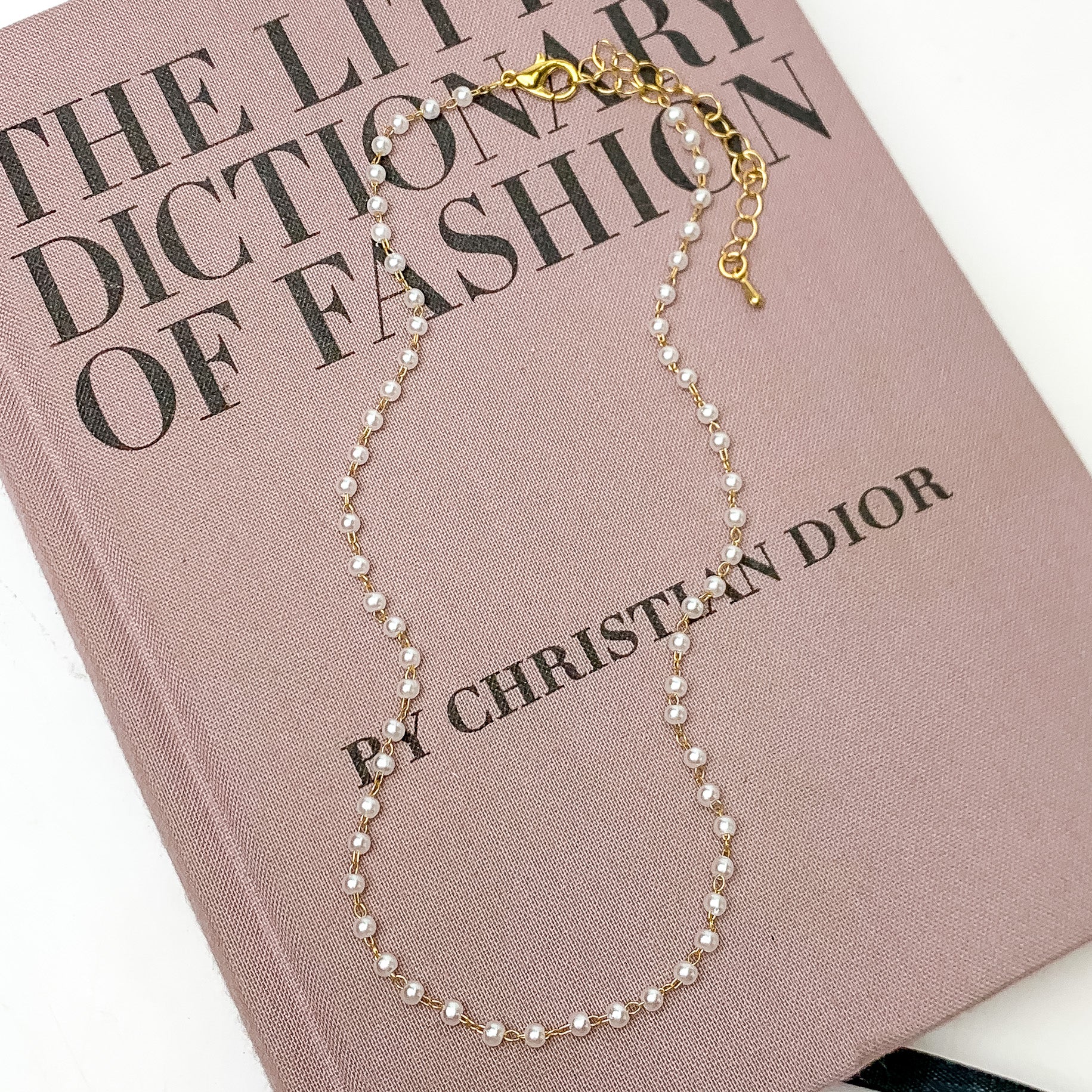 Pearl Linked Necklace in Gold Tone. Pictured on a white background with the necklace laying on a pink book.