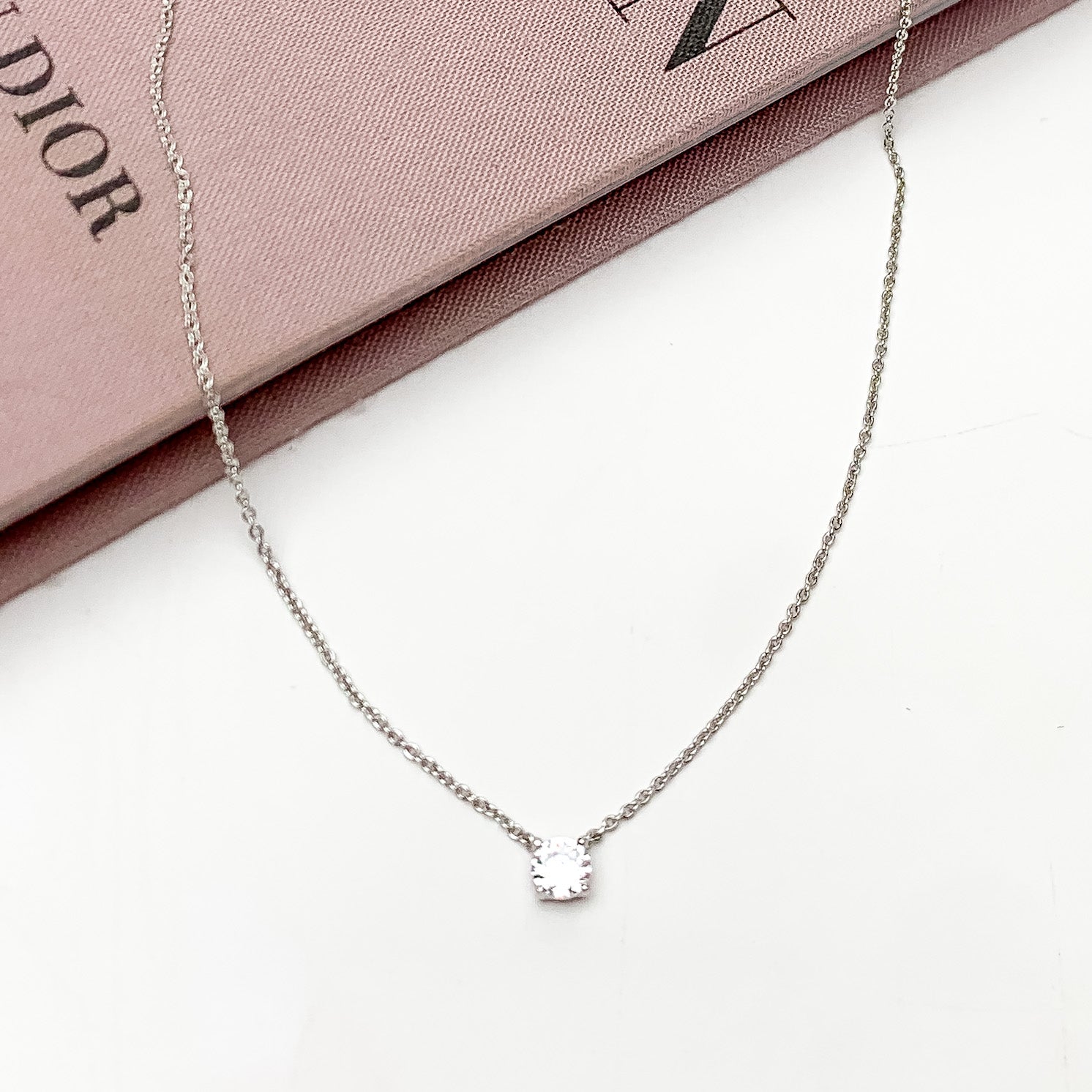 Silver Tone Simple Necklace With Clear Crystal. Pictured on a white background with the top of the necklace on a pink book.