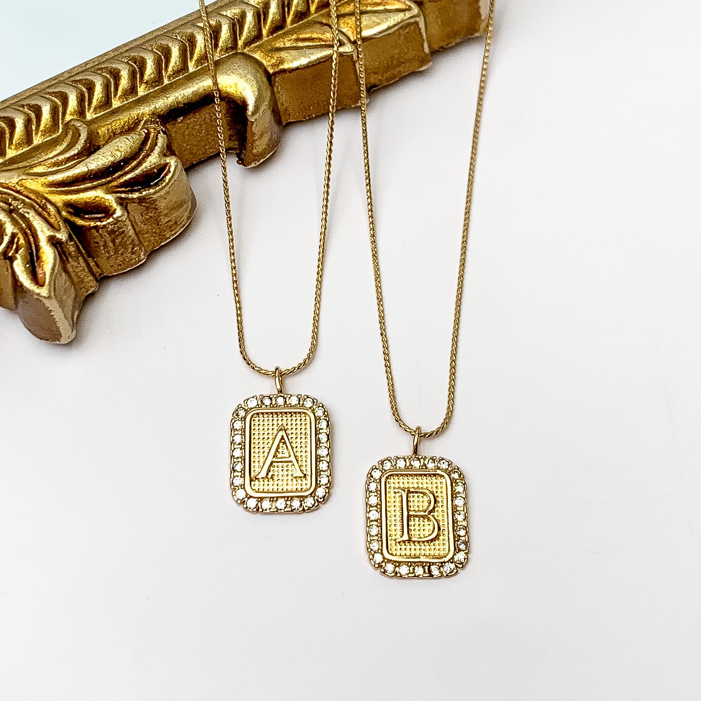 Gold Tone Chain Necklace with Rectangle Initial Pendant Outlined in Clear Crystals. Pictured on a white background with the top of the necklace on a gold frame.