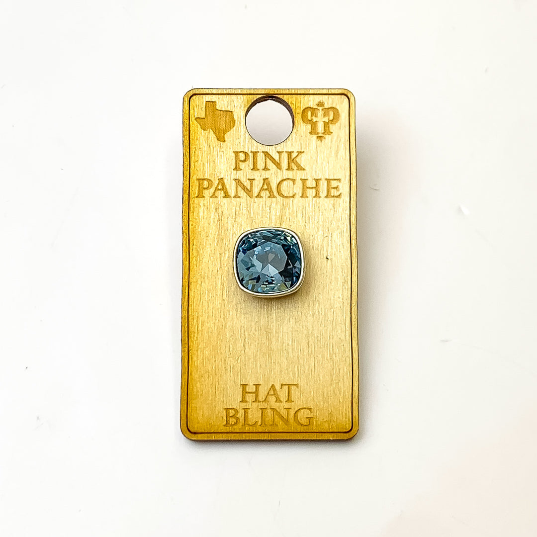 Silver, square hat pin with a denim blue cushion cut crystal. This hat pin is pictured on a wooden Pink Panache holder on a white background.