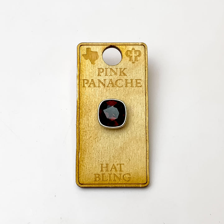 Silver, square hat pin with a maroon cushion cut crystal. This hat pin is pictured on a wooden Pink Panache holder on a white background.