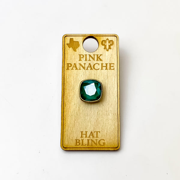 Bronze, square hat pin with a royal green cushion cut crystal. This hat pin is pictured on a wooden Pink Panache holder on a white background.