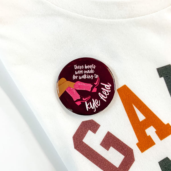 Maroon button pin pictured on a white tee shirt. This pin includes the words "these boots were made for walking to kyle field" in white with pink boots on the side.  