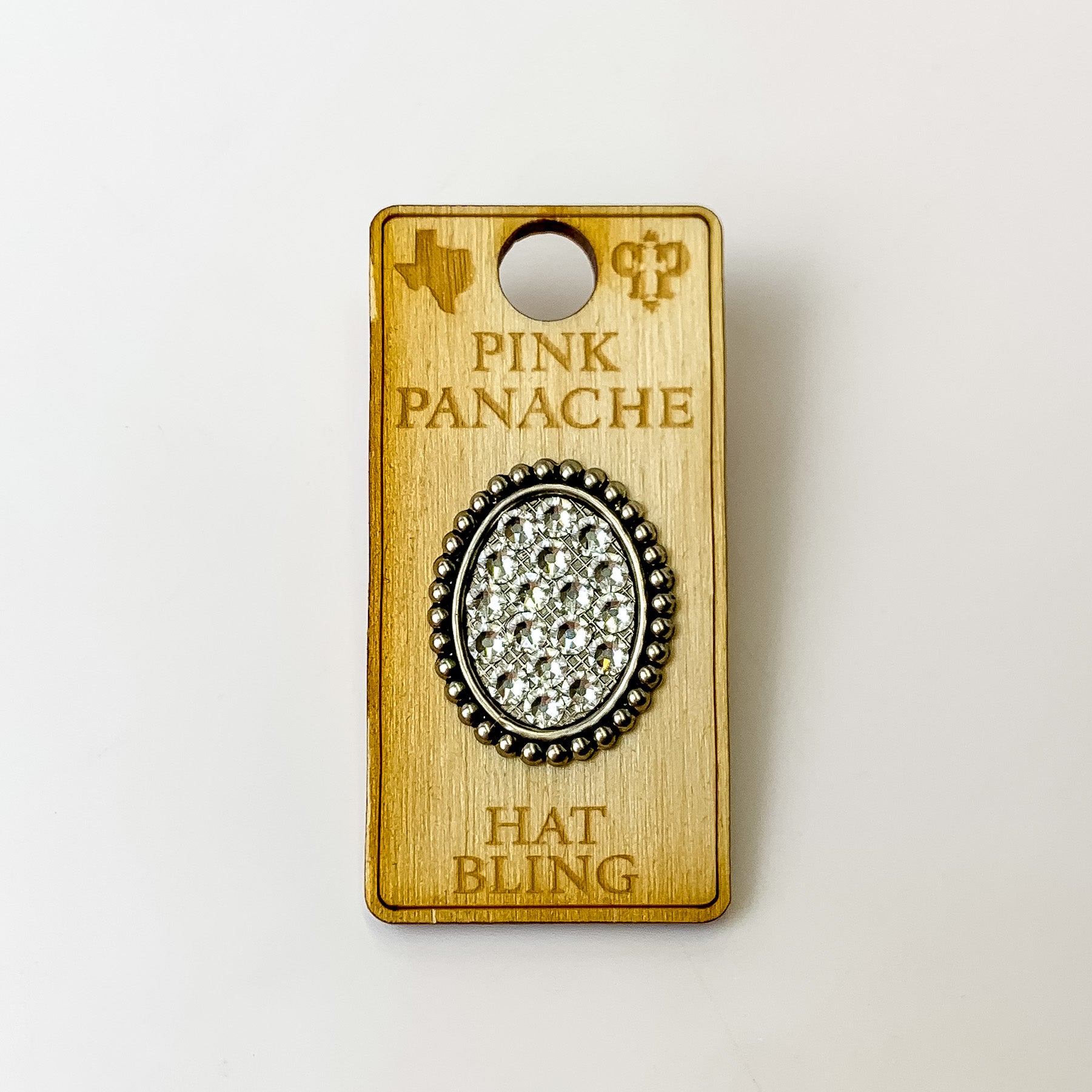 Silver, oval hat pin with a clear crystal inlay. This hat pin is pictured on a wooden Pink Panache holder on a white background.