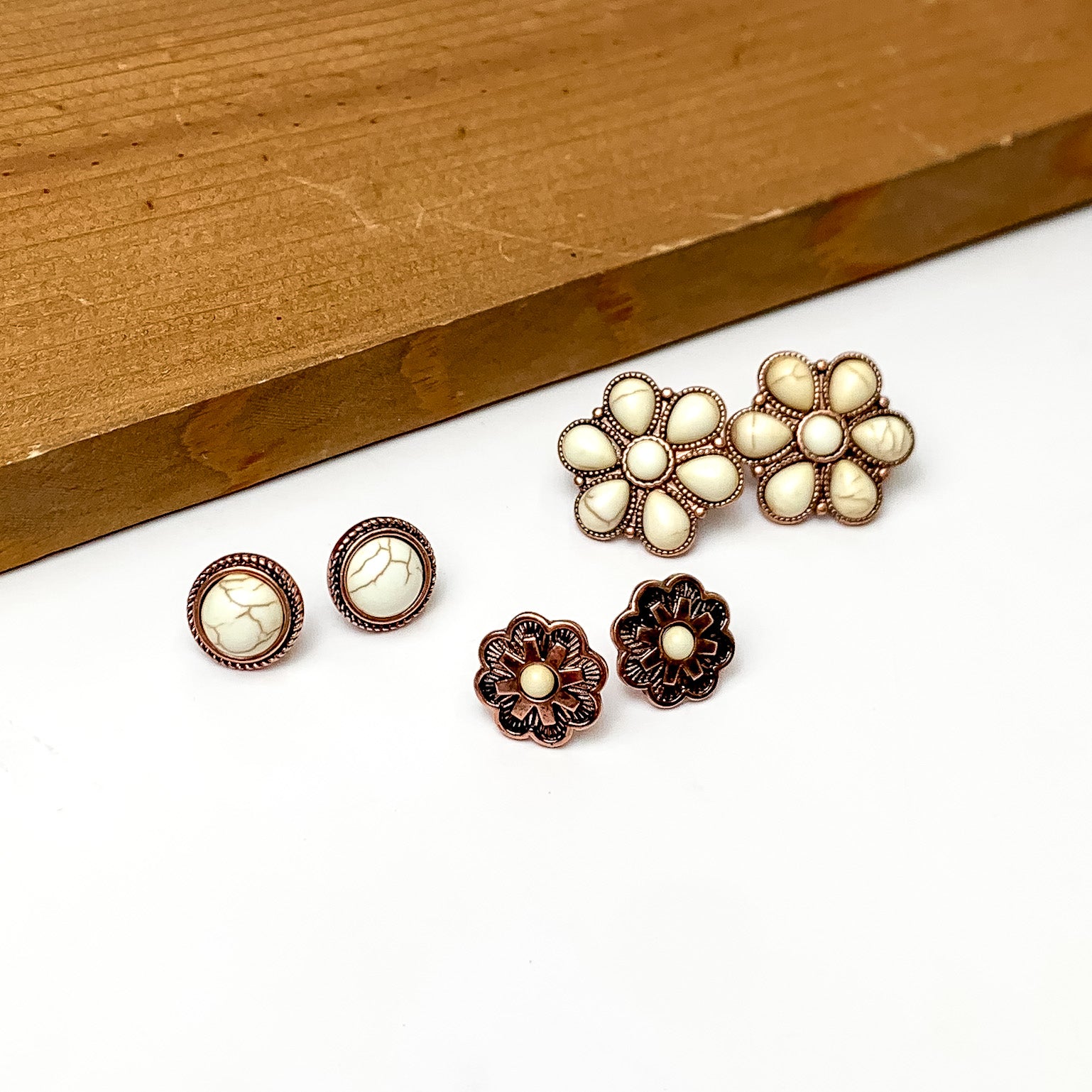 Set Of Three | Multiple Ivory and Copper Tone Stud Earrings. Pictured on a white background with a wood piece above the earrings.