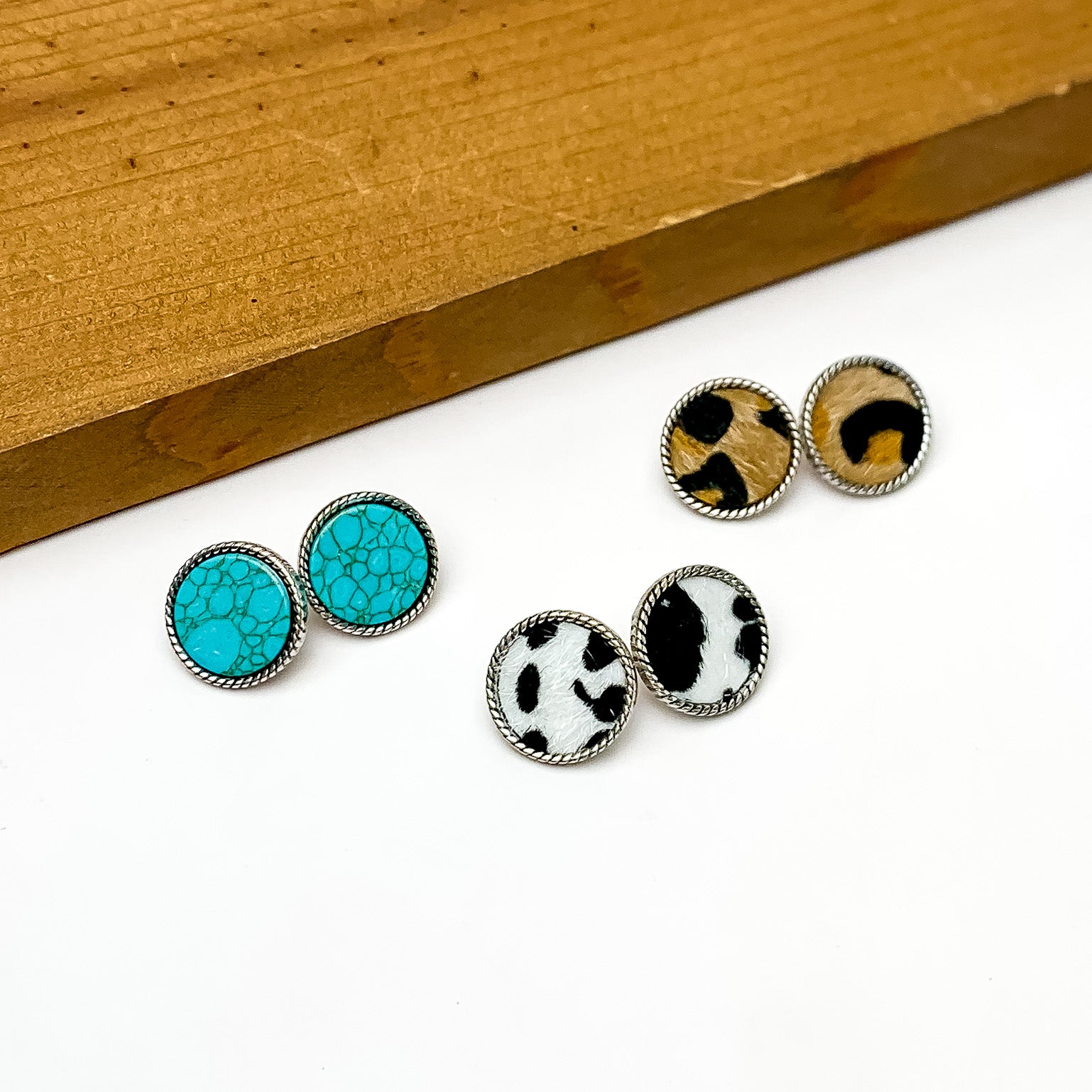 Set Of Three | Multiple Circular Stud Earrings Outlined in Silver Tone. Pictured on a white background with a wood piece above the earrings.
