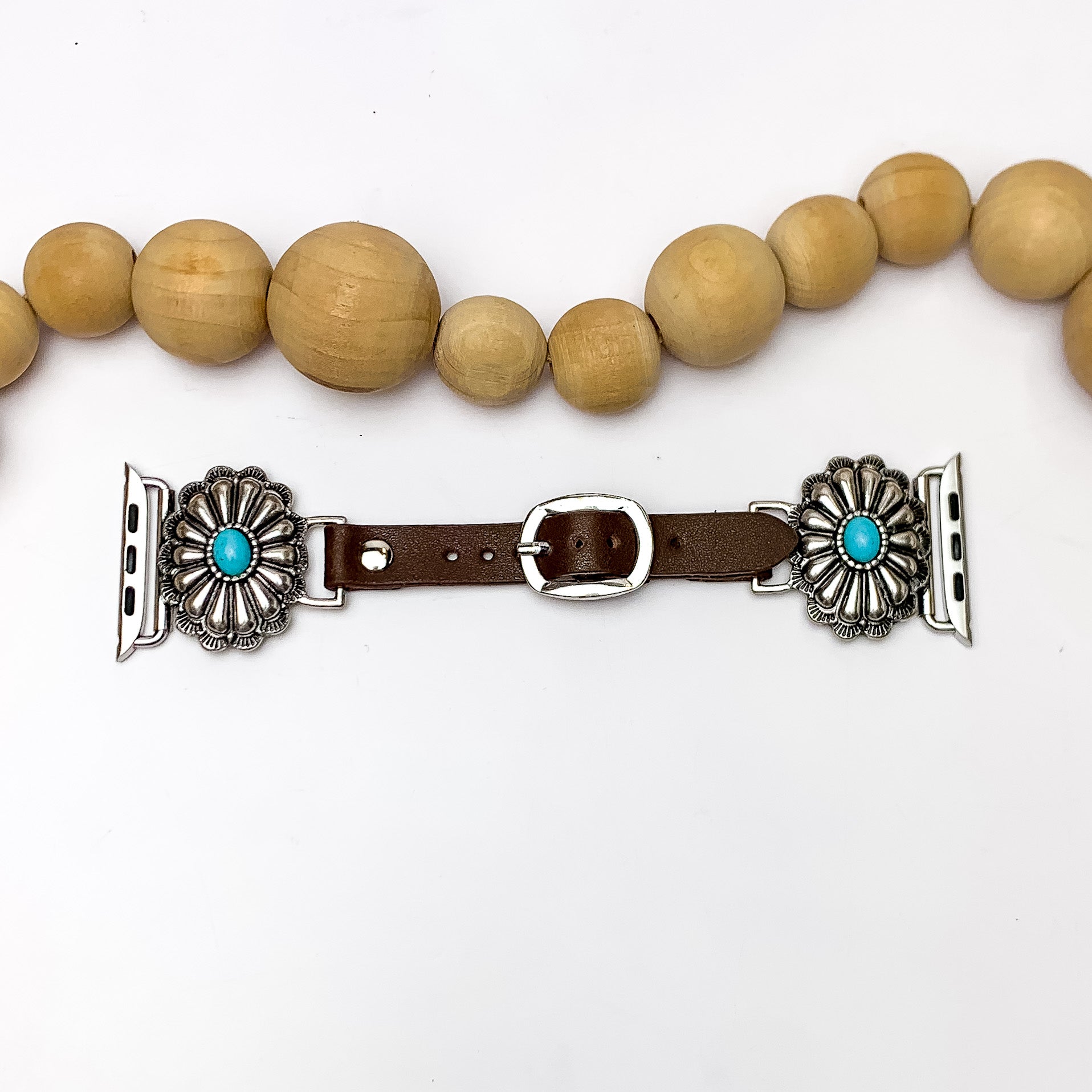 Brown Watch Band with Oval Silver Tone Design and Turquoise Stone. Pictured on a white background with wood beads above the watch for decoration.