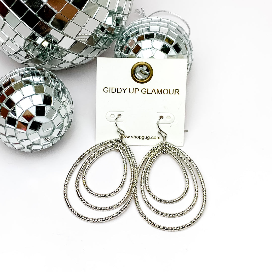 Really Radiant Triple Open Teardrop Earrings in Silver Tone. Pictured on a white background with disco balls in the top left corner.