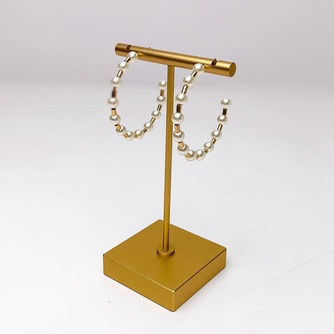 Pretty Pearl Medium Hoop Earrings in Gold Tone. Pictured on a gold platform with a white background.