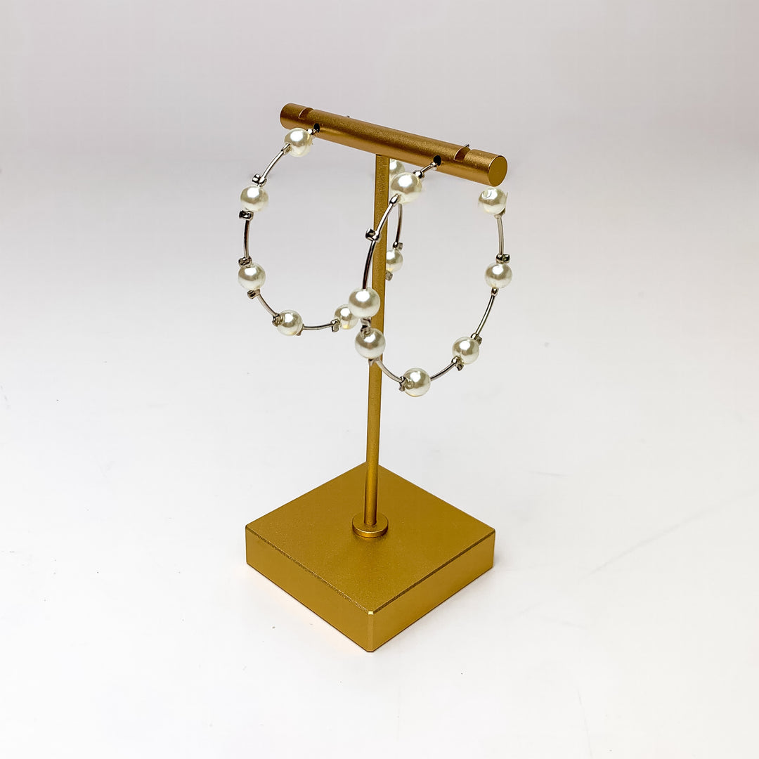 Pearl Paradise Hoop Earrings in Silver Tone. Pictured dangling from a gold holder with a white background.