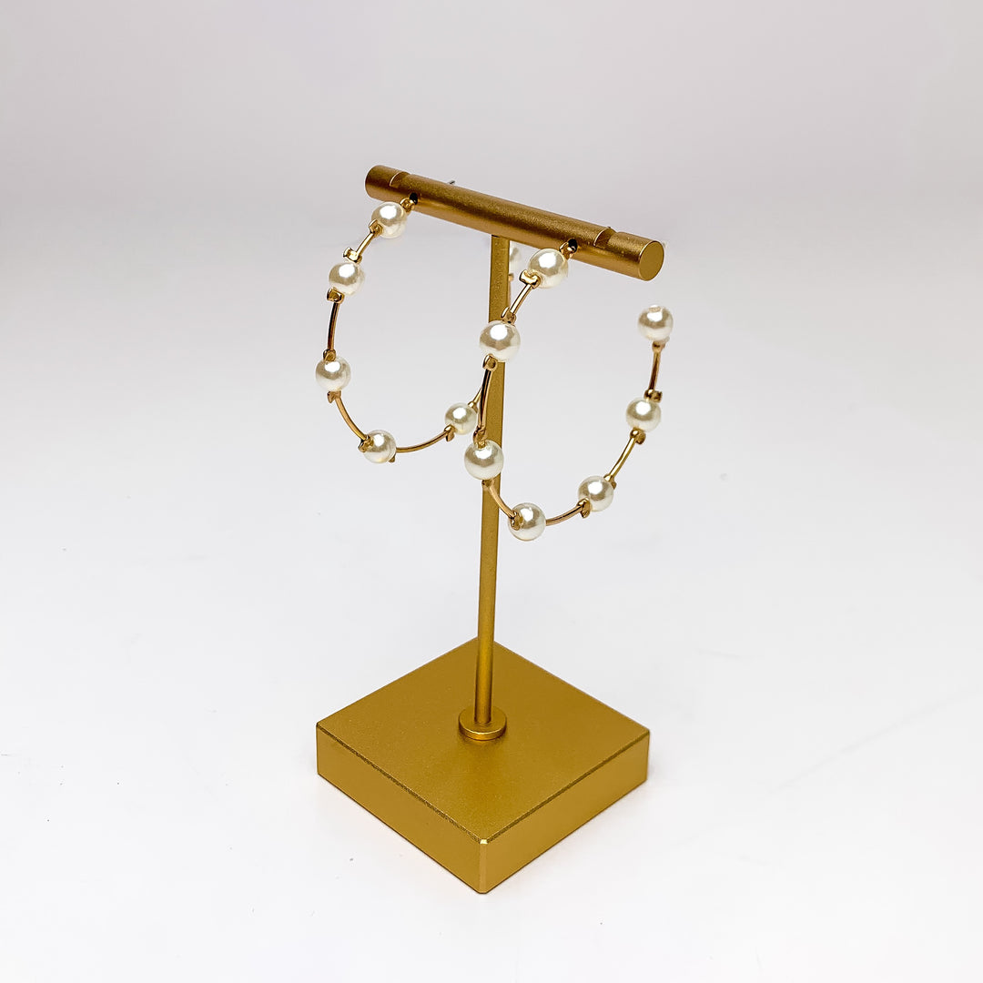 Pearl Paradise Hoop Earrings in Gold Tone. Pictured dangling from a gold holder with a white background.