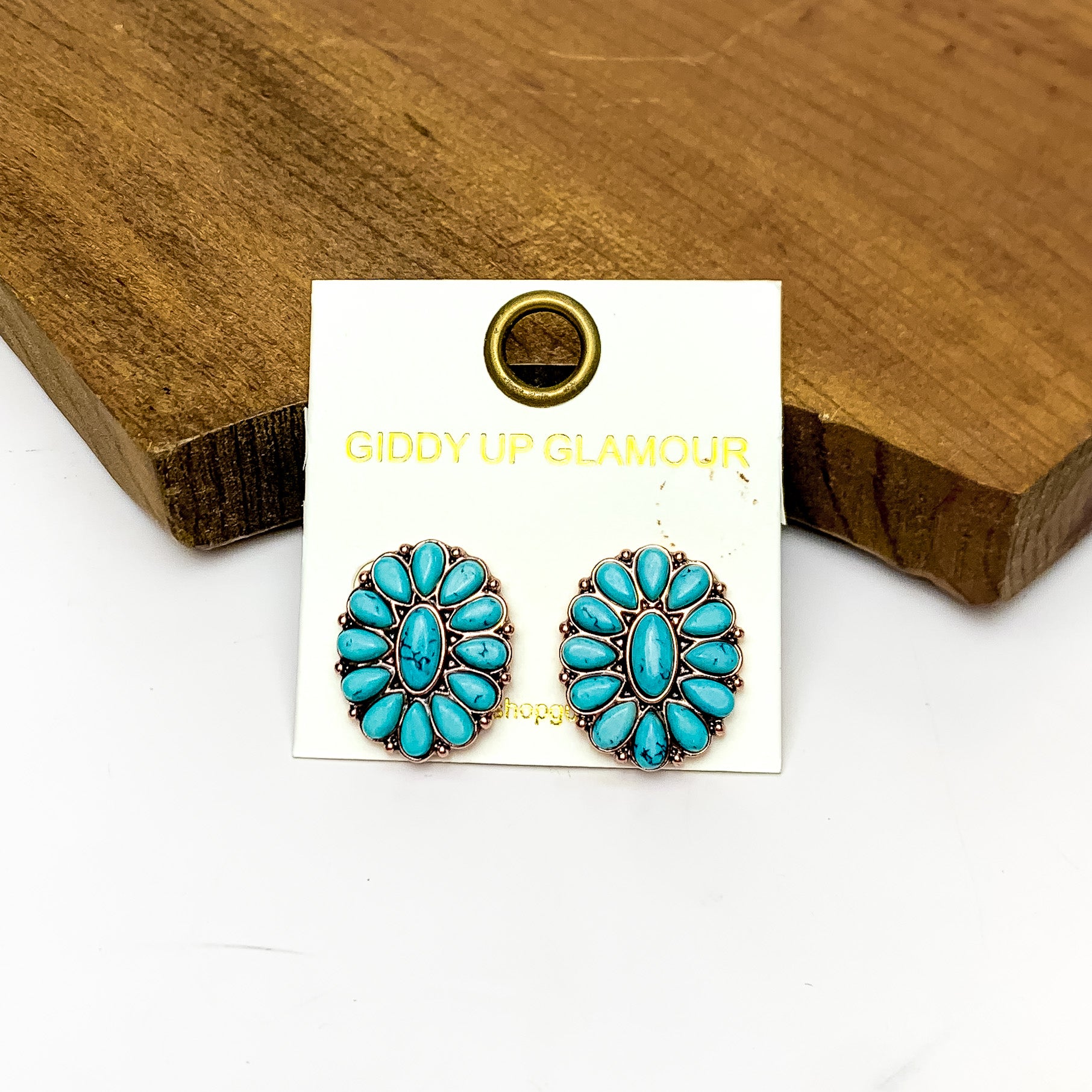 Copper Tone Concho Cluster Oval Earrings in Turquoise Blue. Pictured on a white background with the earrings laying against a wood piece.