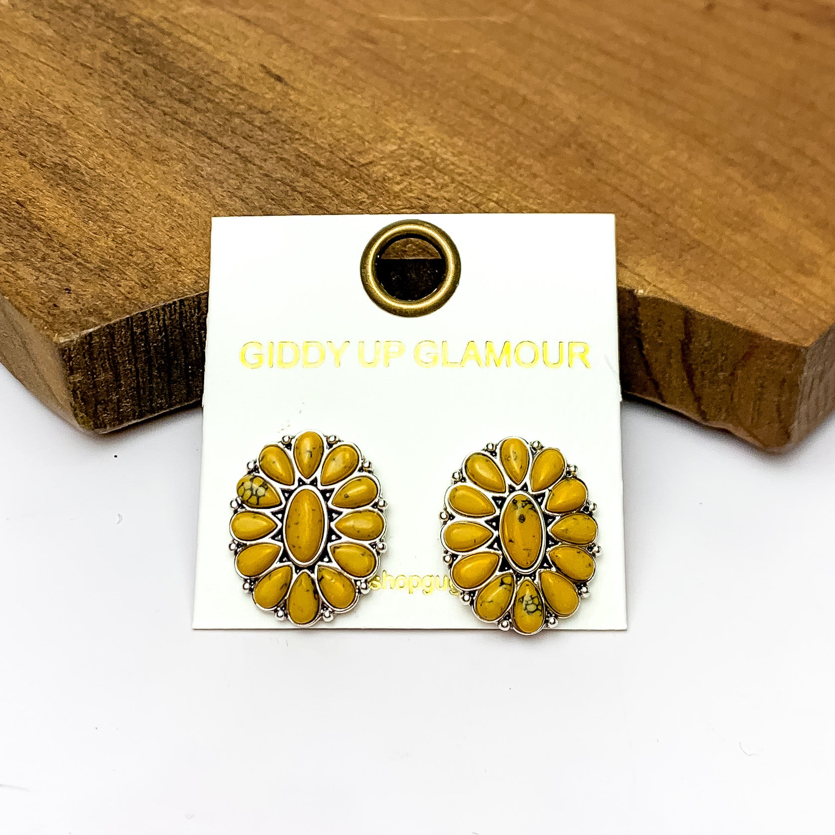 Silver Tone Concho Cluster Oval Earrings in Yellow. Pictured on a white background with the earrings laying against a wood piece.