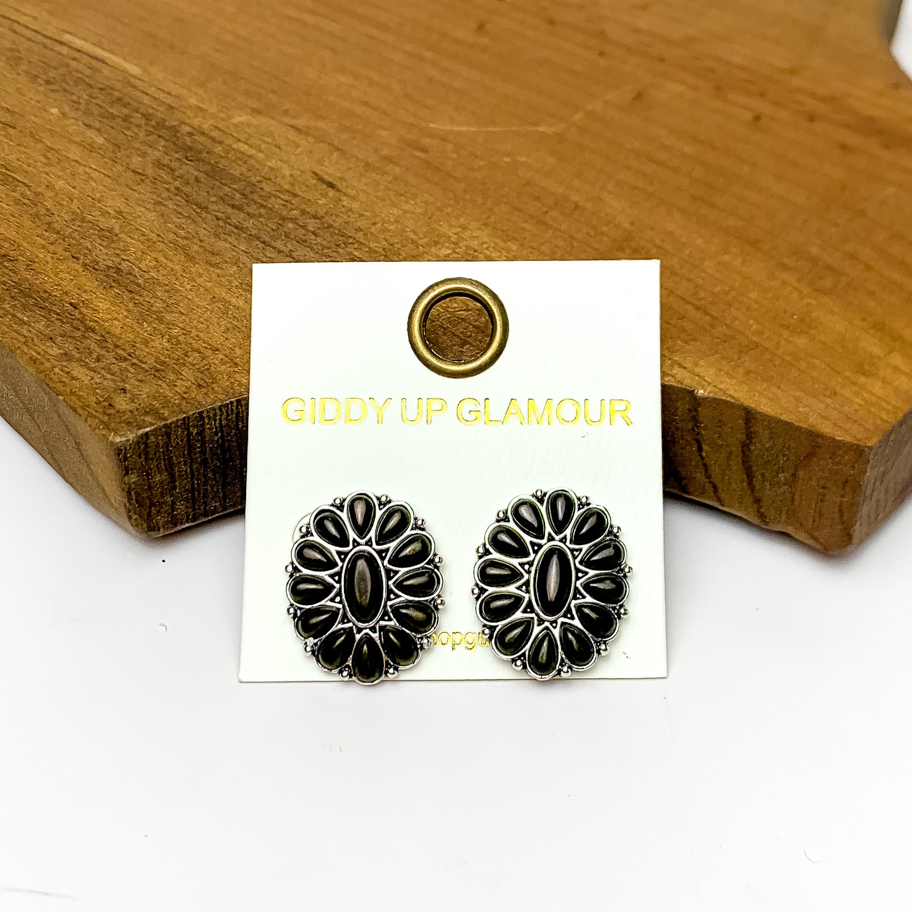 Silver Tone Concho Cluster Oval Earrings in Black. Pictured on a white background with the earrings laying against a wood piece.