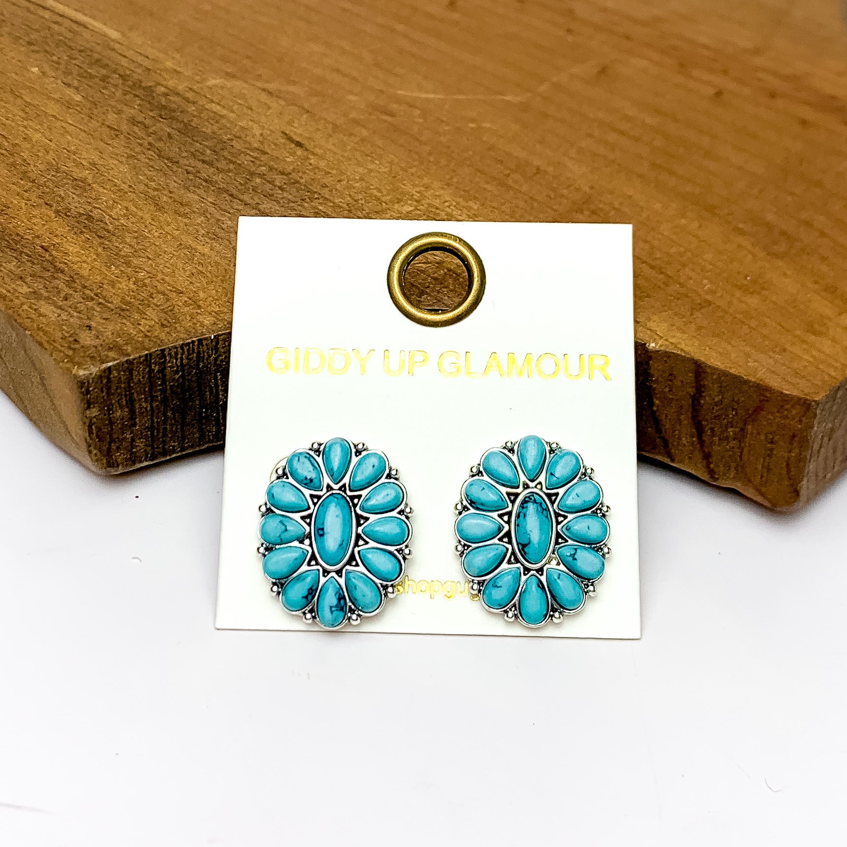 Silver Tone Concho Cluster Oval Earrings in Turquoise. Pictured on a white background with the earrings laying against a wood piece.