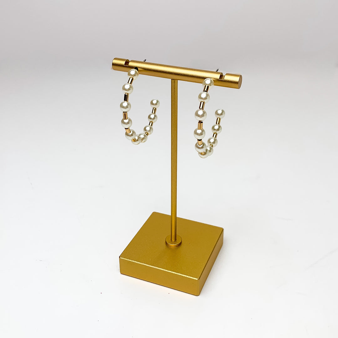 Pretty Pearl Small Hoop Earrings in Gold Tone. Pictured on a gold platform with a white background.