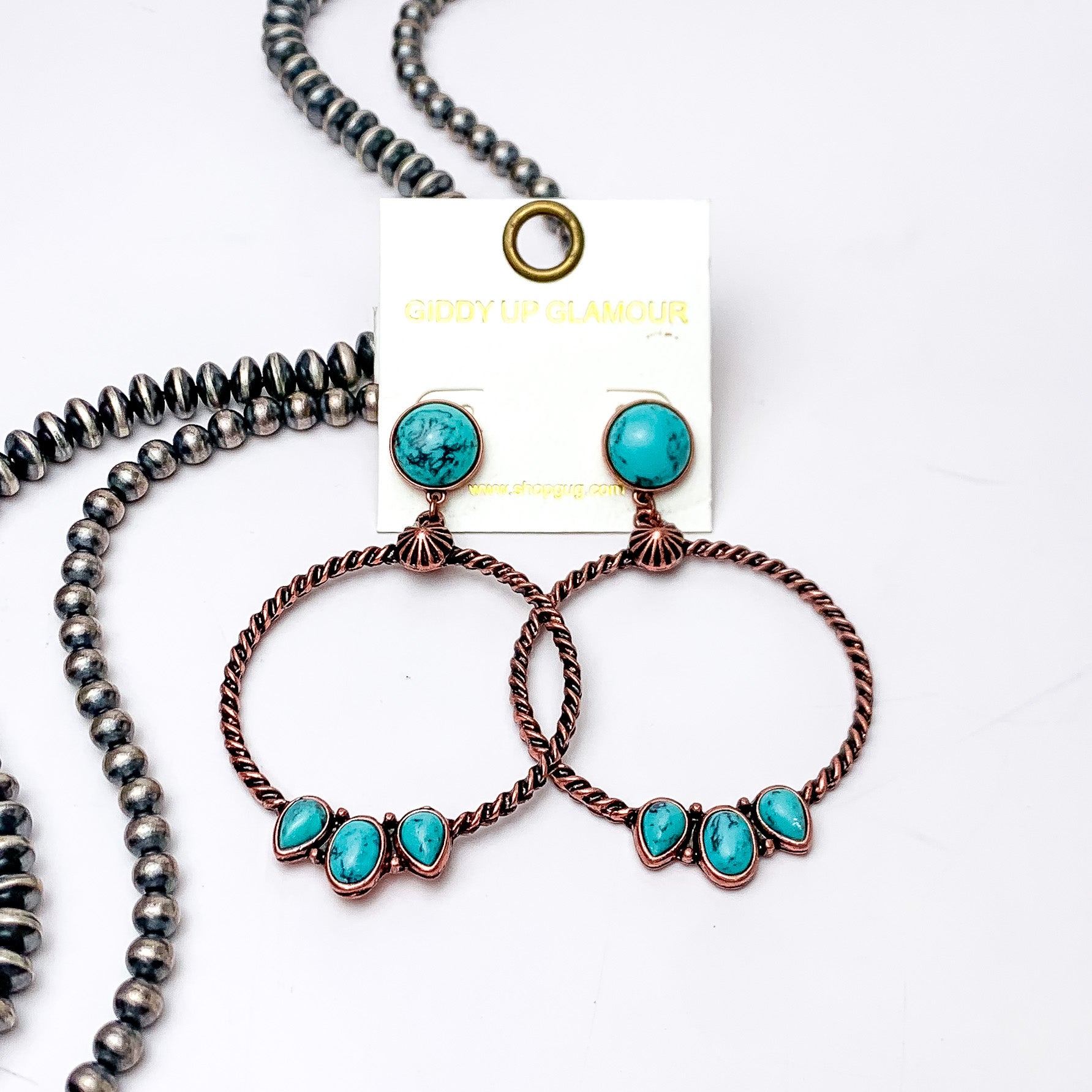 Circle, turquoise stone post earrings with a copper circle drop pendant. At the bottom of the circle there are three different shaped stones in turquoise. These earrings are pictured on a white background with silver beads on the left side bottom of the picture. 