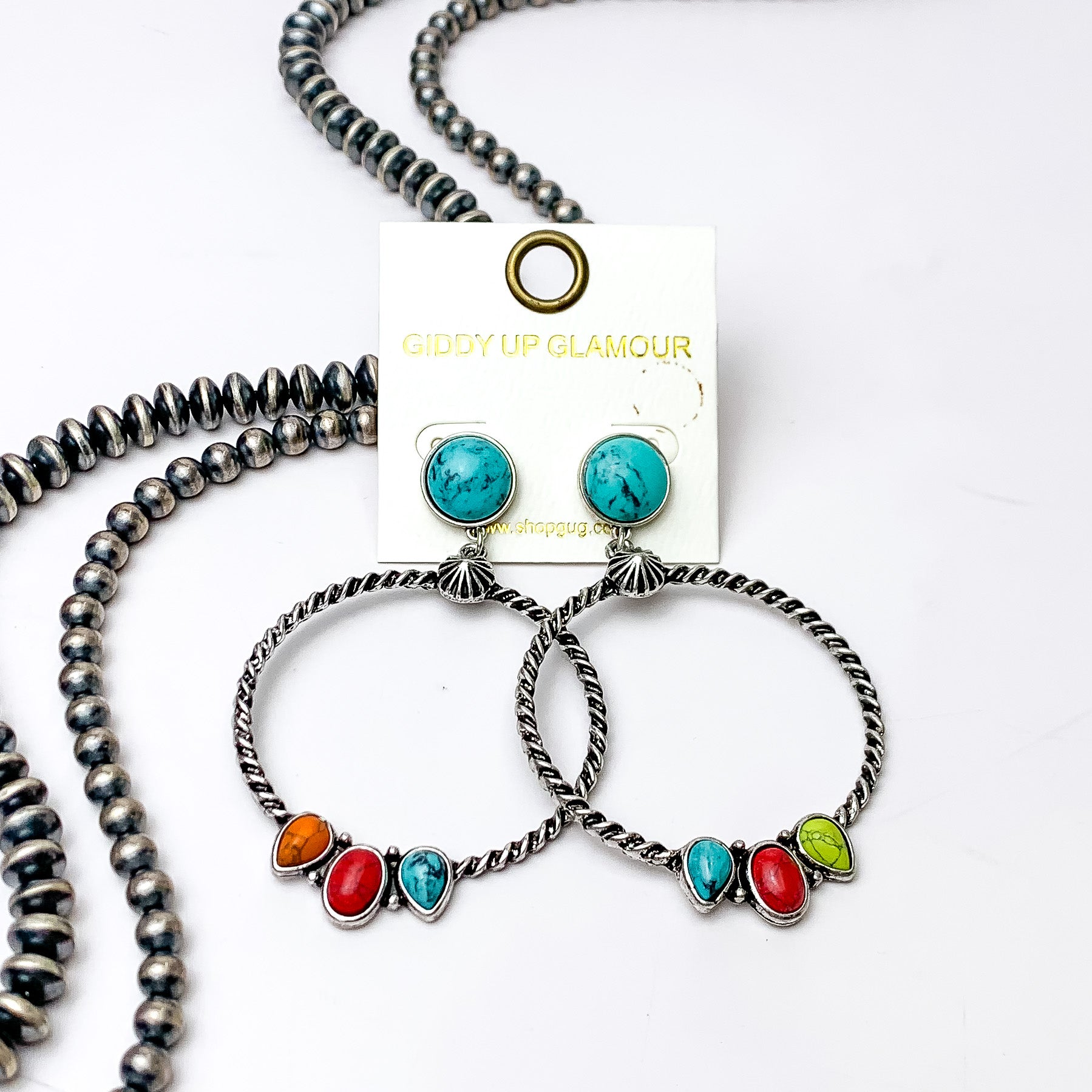 Circle, turquoise stone post earrings with a copper circle drop pendant. At the bottom of the circle there are three different shaped stones in multicolor. These earrings are pictured on a white background with silver beads on the left side bottom of the picture. 