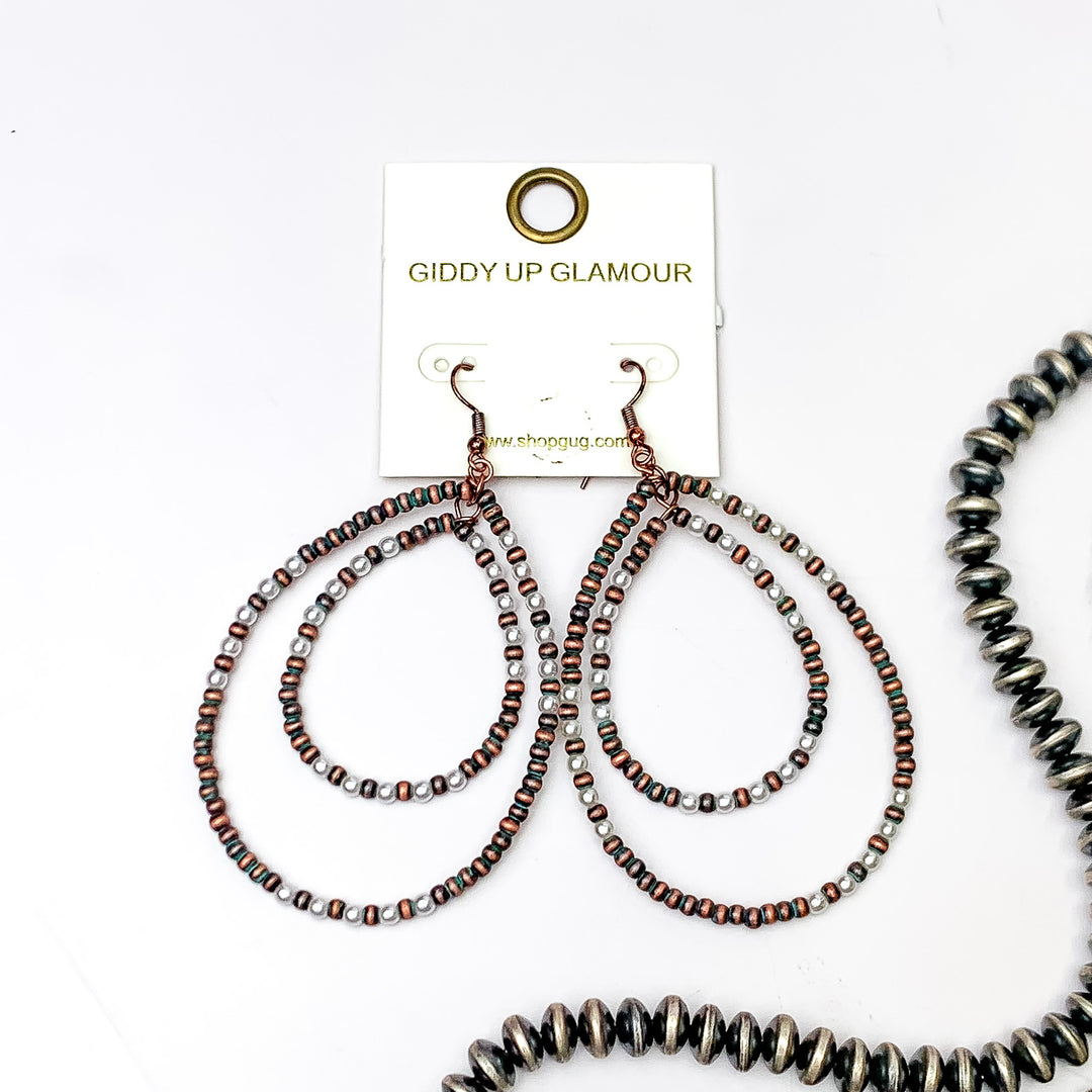 Double teardrop beaded earrings with patina and white beads, These earrings are pictured on a white background with silver beads on the right side bottom of the picture. 