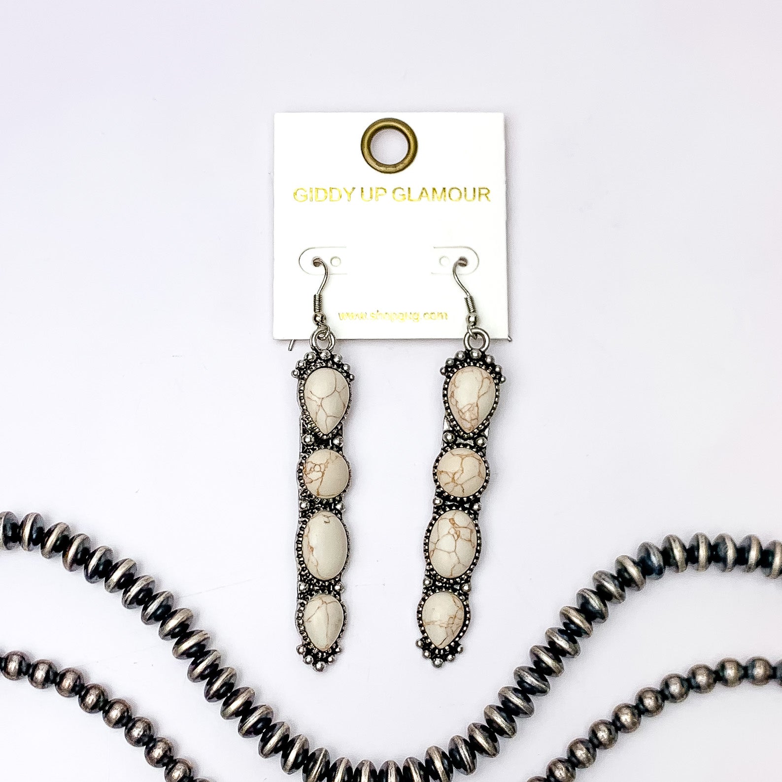 Silver fish hook earrings with a four, ivory stone pendant. These earrings are pictured on a white background with silver beads at the bottom of the picture. 