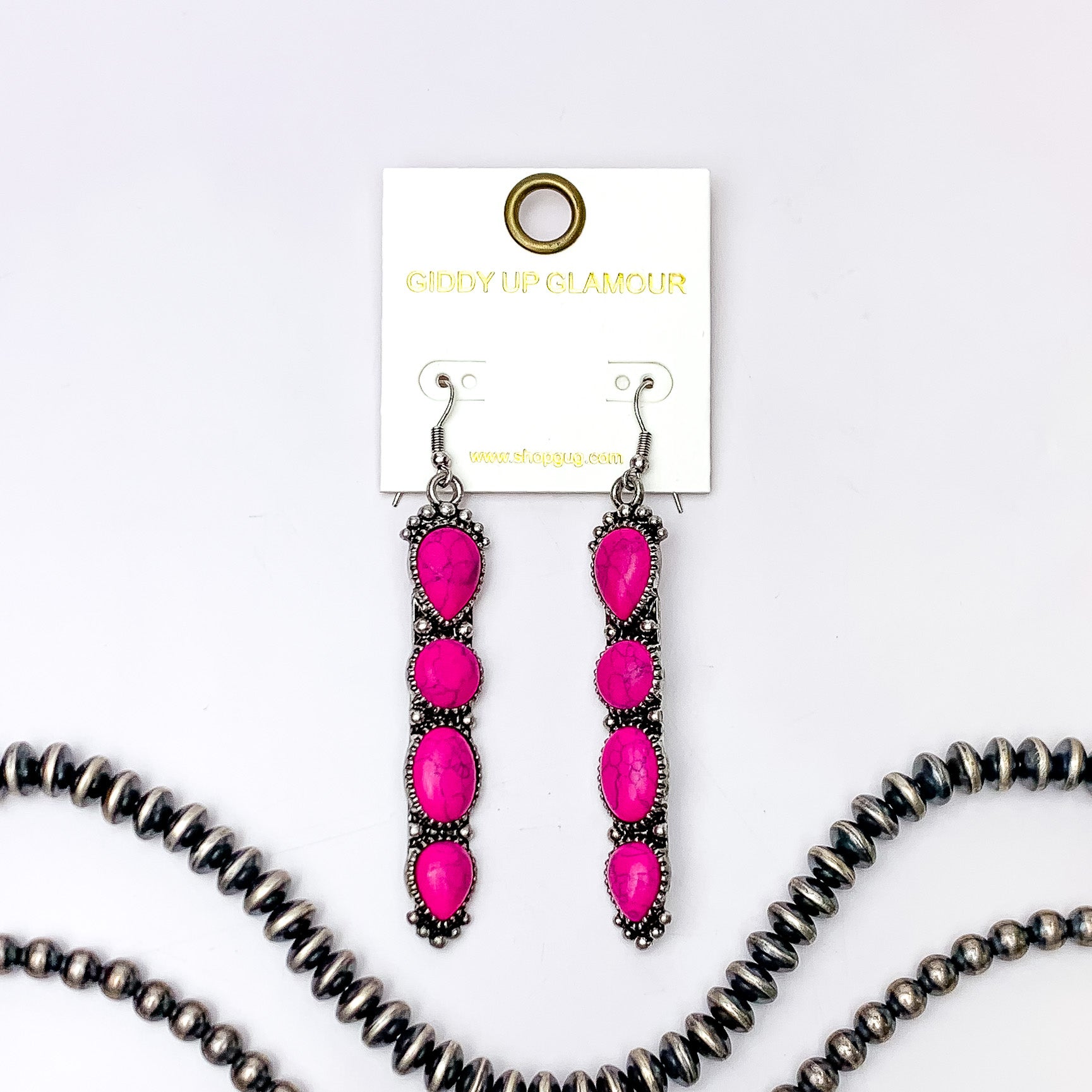 Silver fish hook earrings with a four, fuchsia pink stone pendant. These earrings are pictured on a white background with silver beads at the bottom of the picture. 