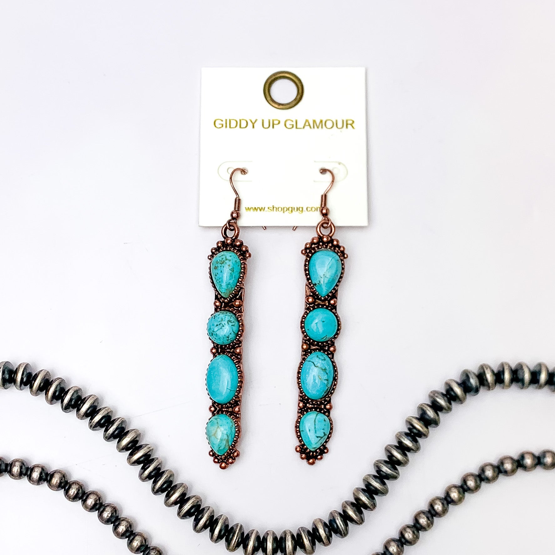 Copper fish hook earrings with a four, turquoise stone pendant. These earrings are pictured on a white background with silver beads at the bottom of the picture. 