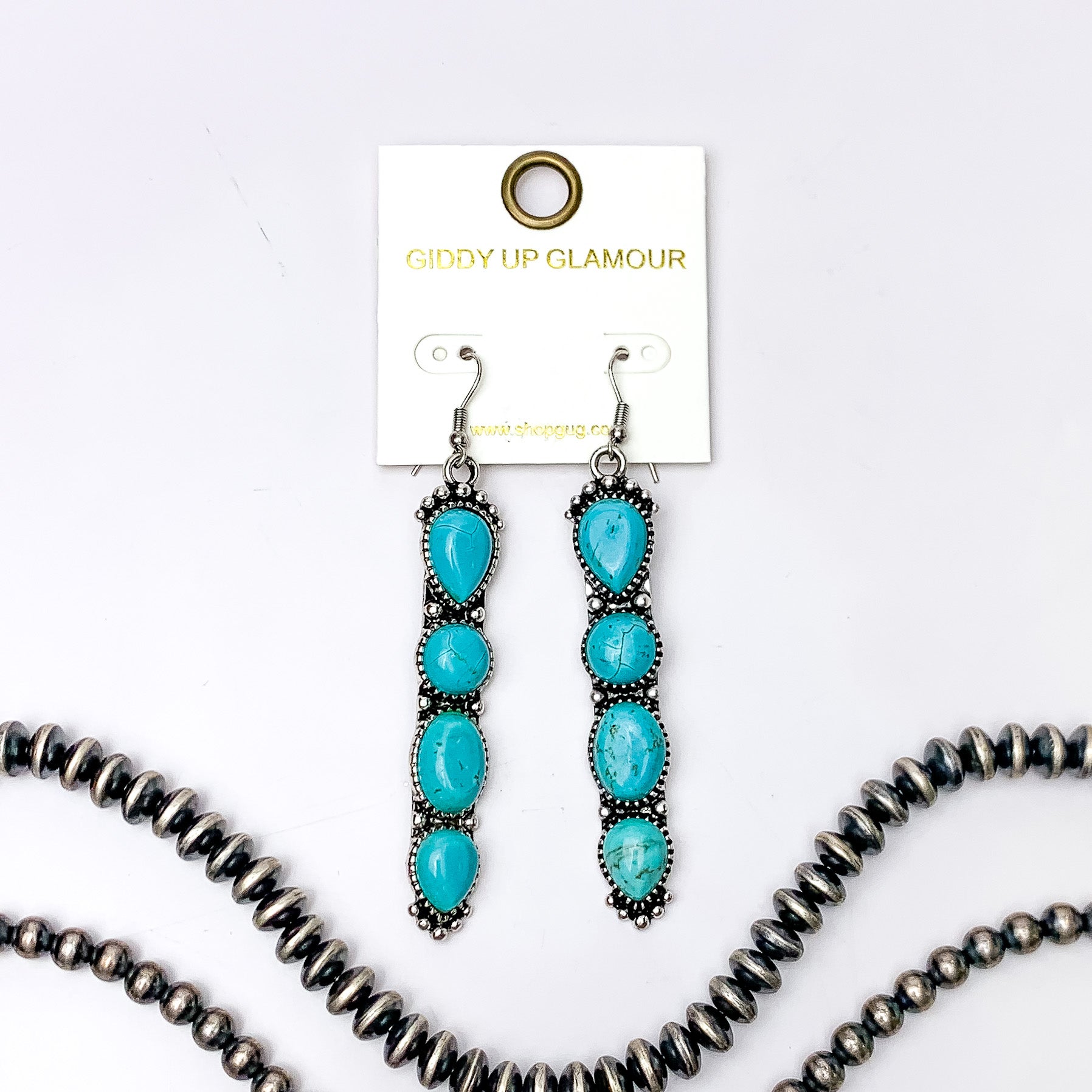 Silver fish hook earrings with a four, turquoise stone pendant. These earrings are pictured on a white background with silver beads at the bottom of the picture. 