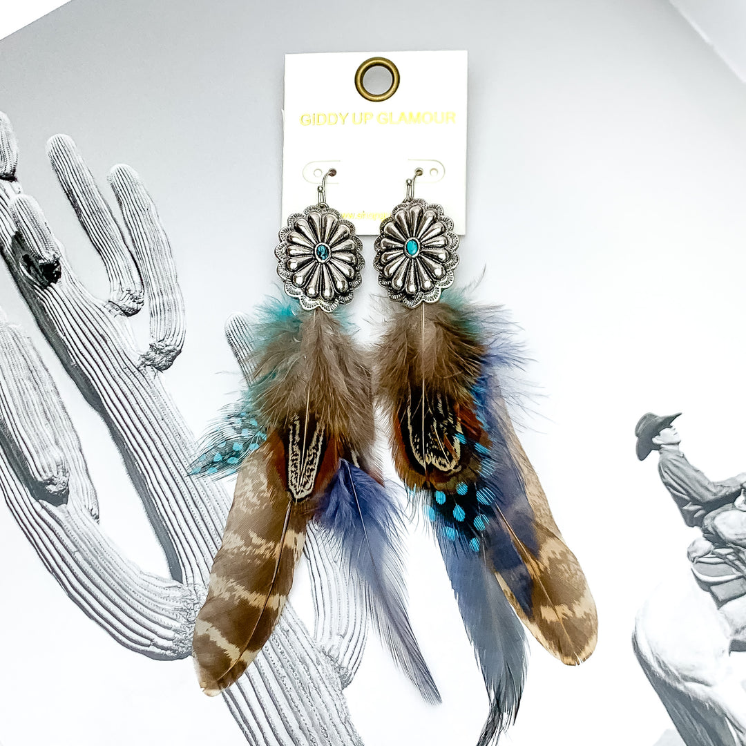 Desert Doll Silver Tone Feather Earrings in dark blue. Pictured on an open western book.