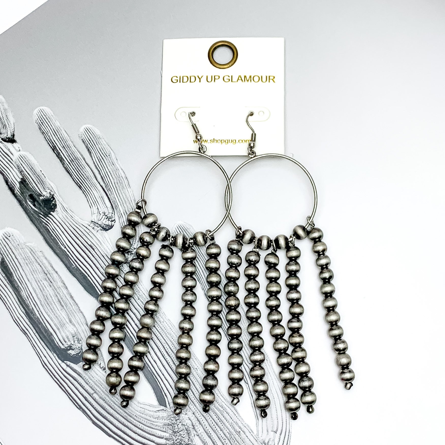 Silver hoop earrings with beaded tassels in silver. These earrings are pictured on a black and white picture. 