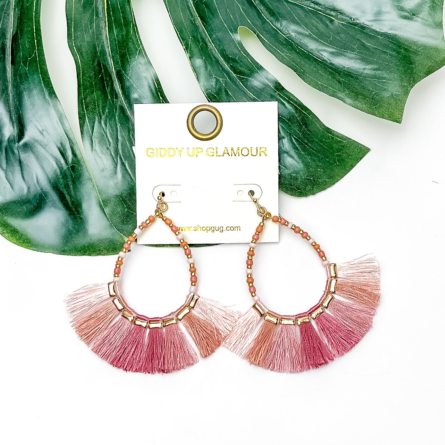 Beaded Open Teardrop Earrings With Fringe Bottom in Pink Tones. Pictured ono a white background with a leaf behind the earrings.