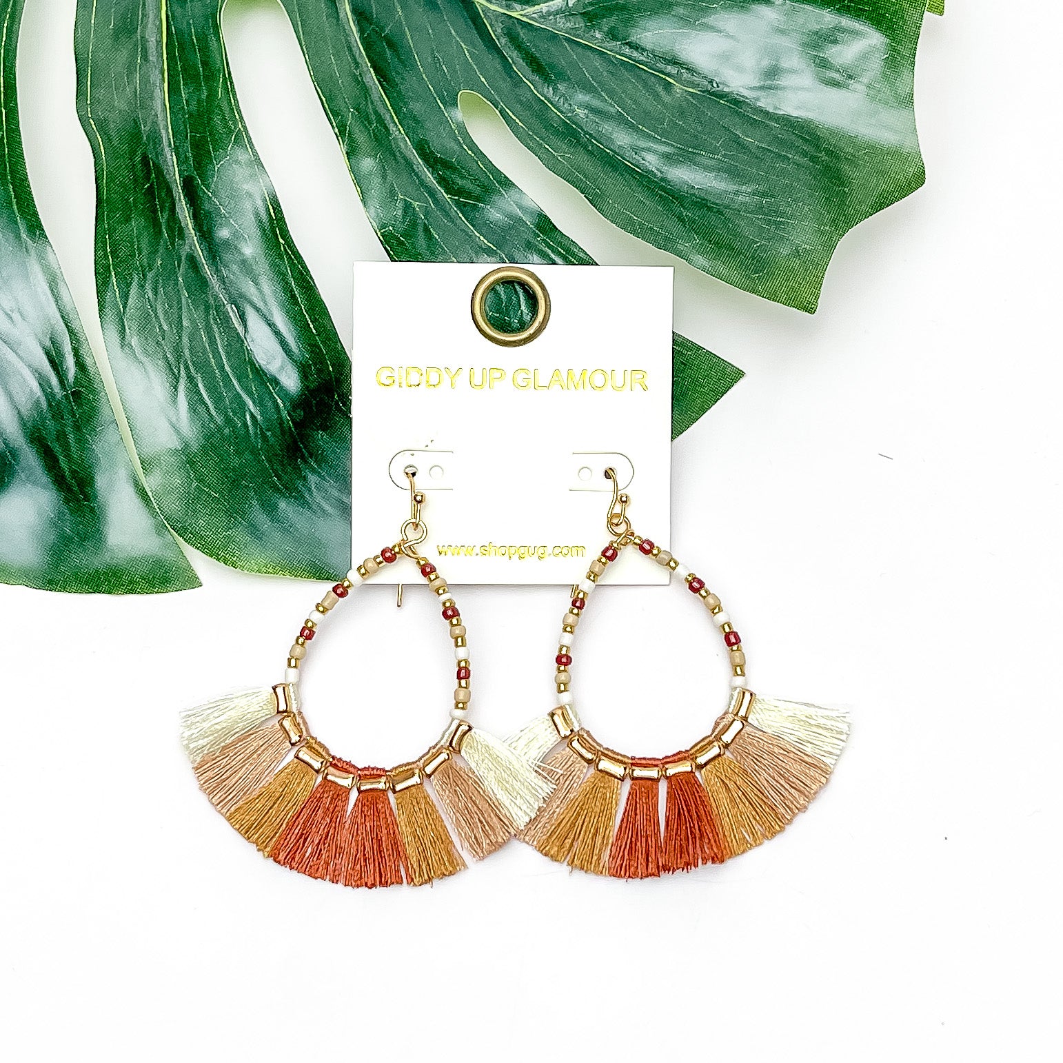 Beaded Open Teardrop Earrings With Fringe Bottom in Neutral Tones. Pictured on a white background with a leaf behind the earrings.