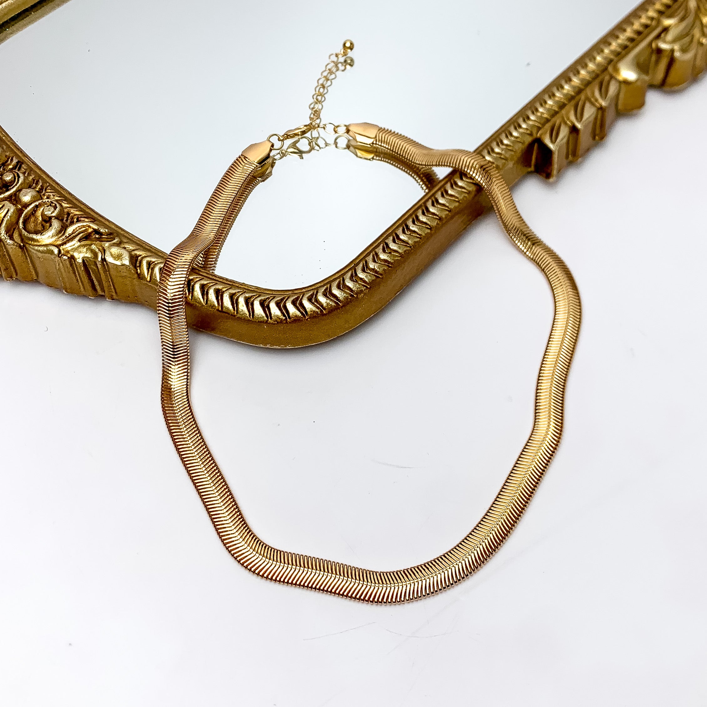 Daily Basis Gold Tone Chain Necklace. Pictured on a white background with part of the necklace on a mirror with a gold frame.