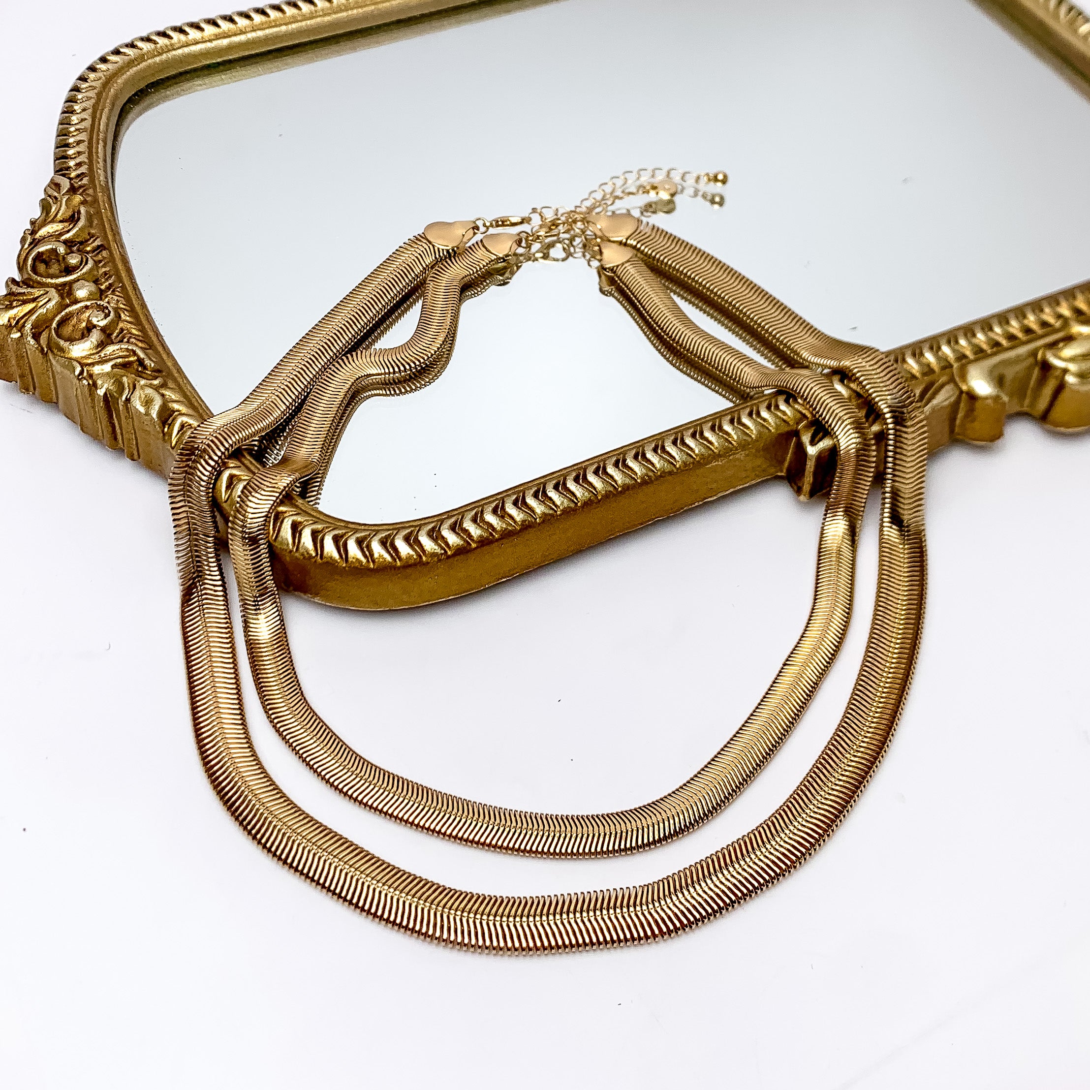 Daily Basis Gold Tone Double Chain Necklace. Pictured on a white background with part of the necklace on a mirror with a gold frame.