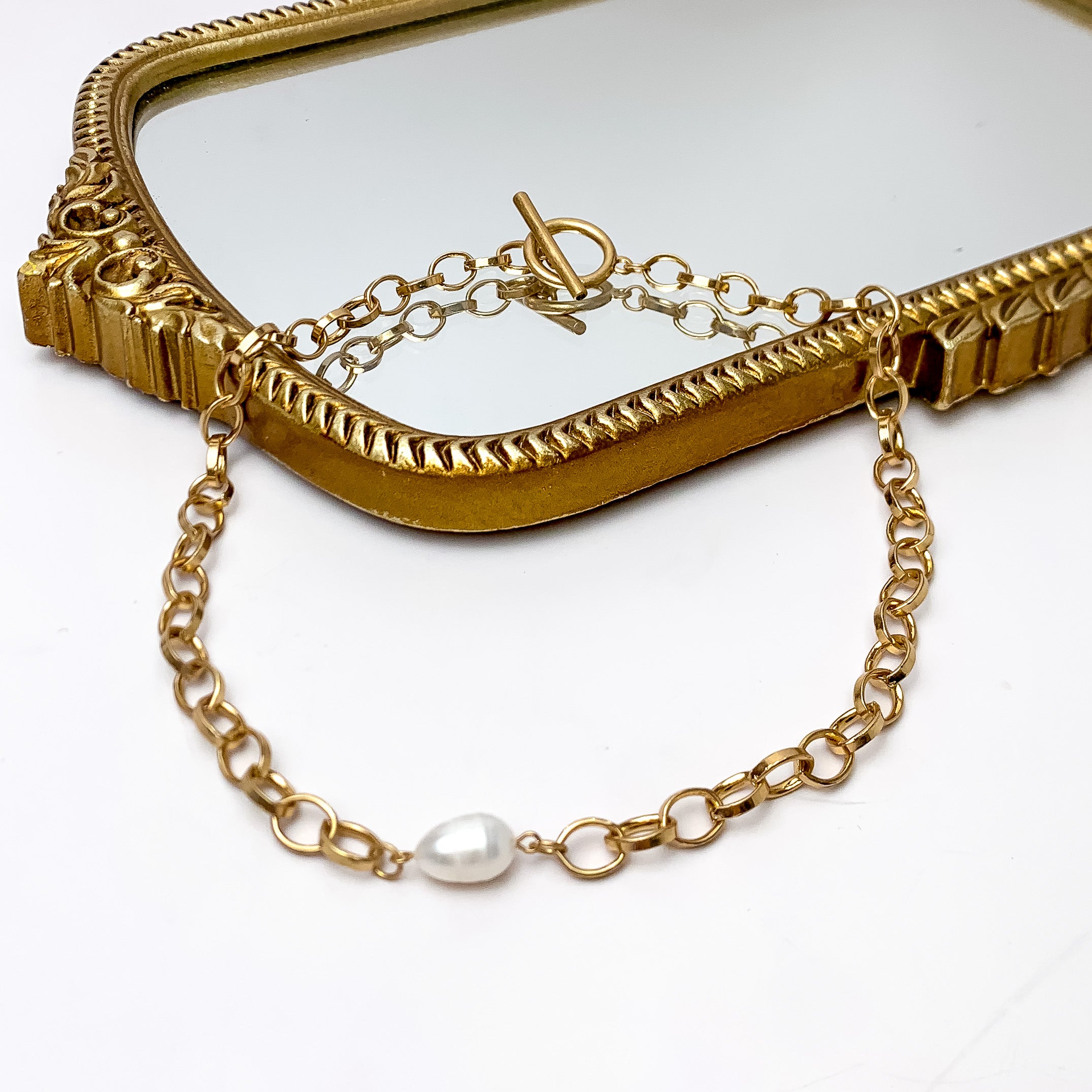 Pearl Accent Gold Tone Chain Necklace With Toggle Clasp. Pictured on a white background with part of it on a gold trimmed mirror.
