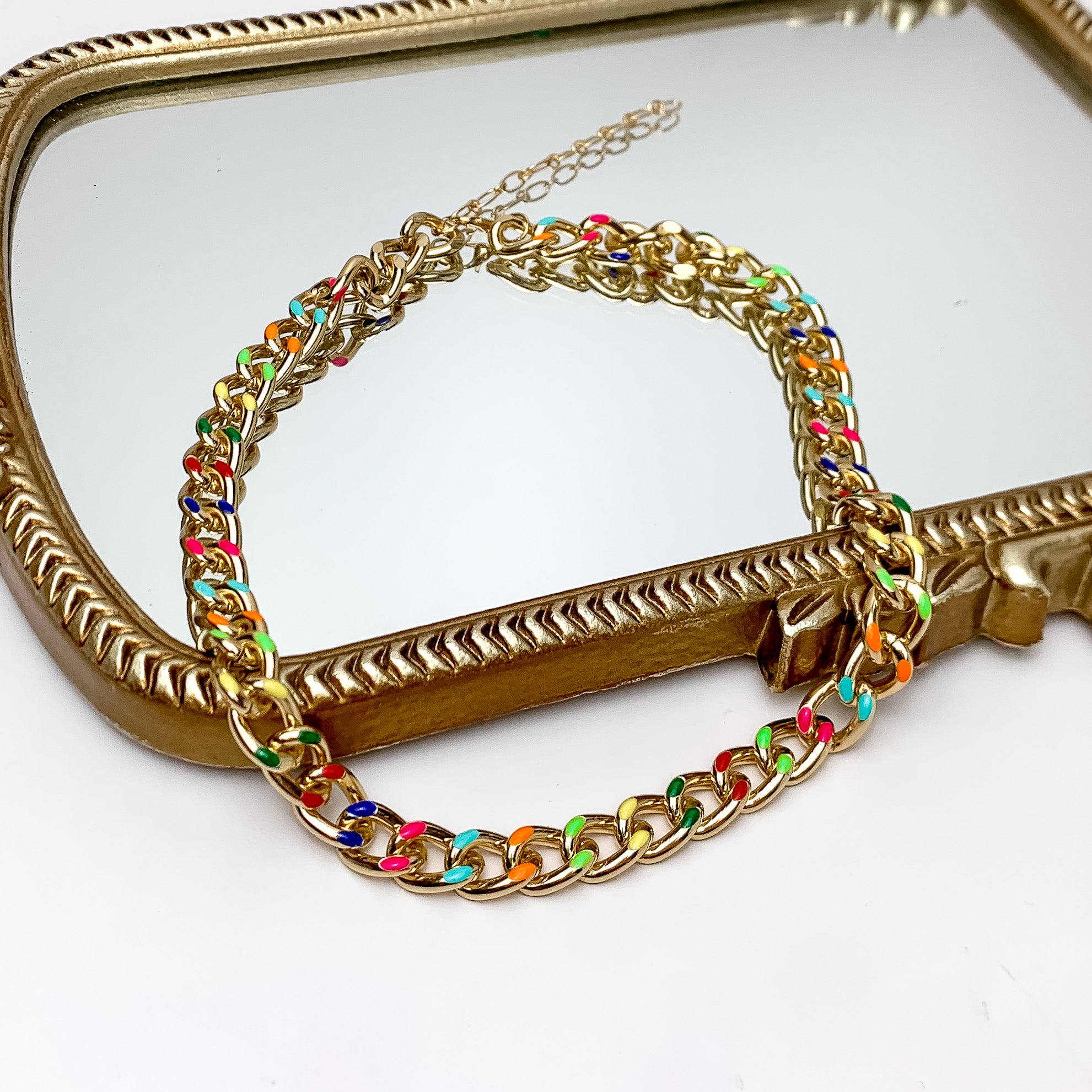 Gold Tone Chain With Accents of Multicolor. Pictured on a white background with part of the necklace on a gold trimmed mirror.