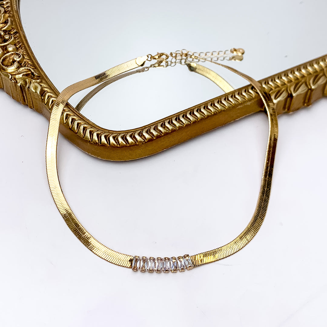 Gold Tone Chain Necklace With Rectangle Clear Crystals. Pictured on a white background with the top part of the necklace on a gold trim mirror.