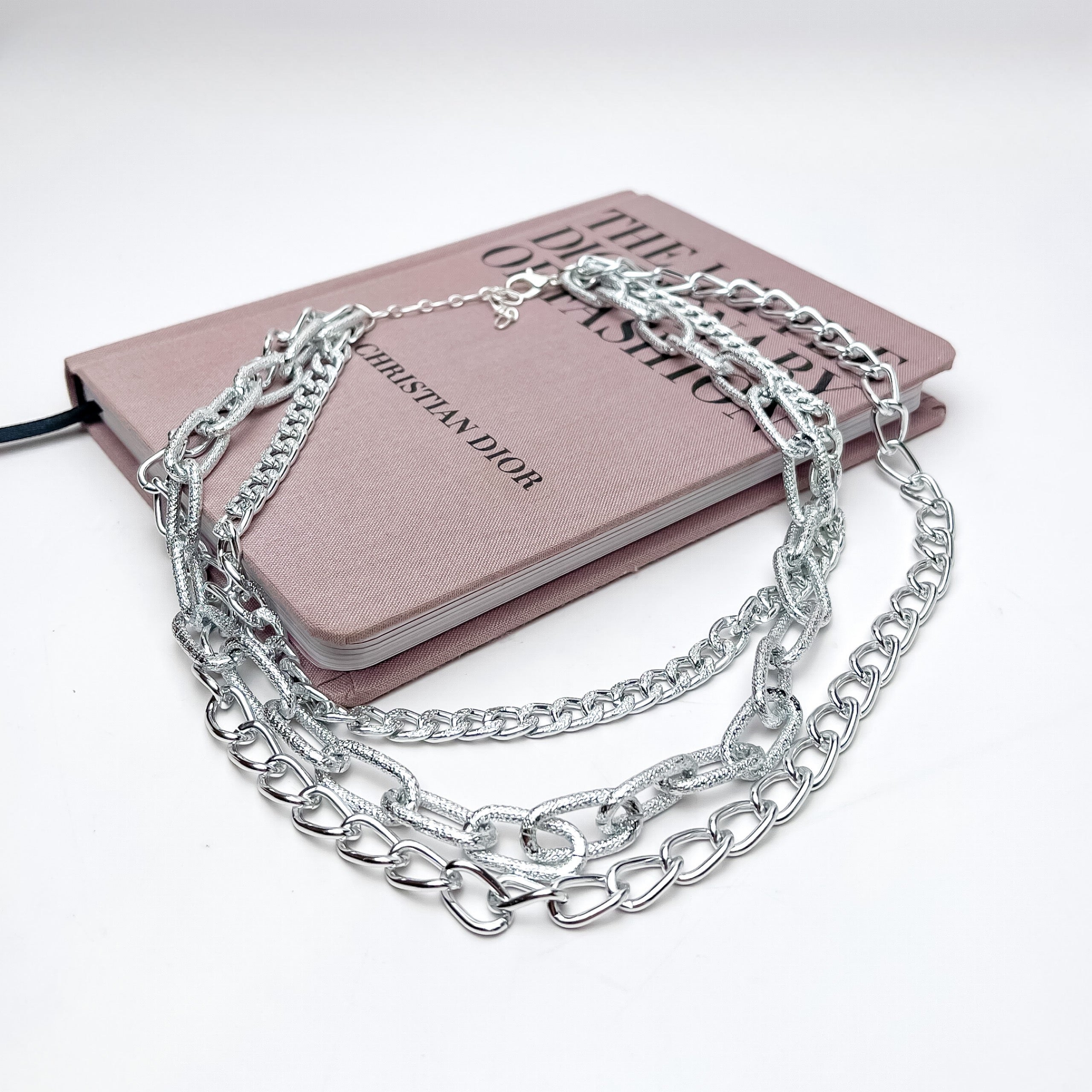 Triple Strand Chunky Chain Silver Tone Necklace. This necklace is putured laying on a pink book with a white background.