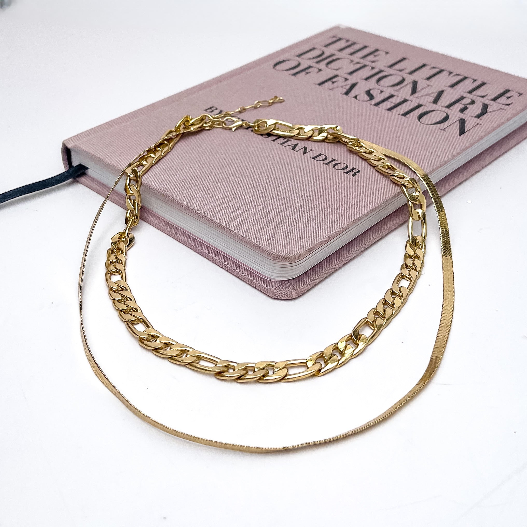 Dinner Date Double Strand Gold Tone Necklace. This necklace is pictured on a pink book with a white background.