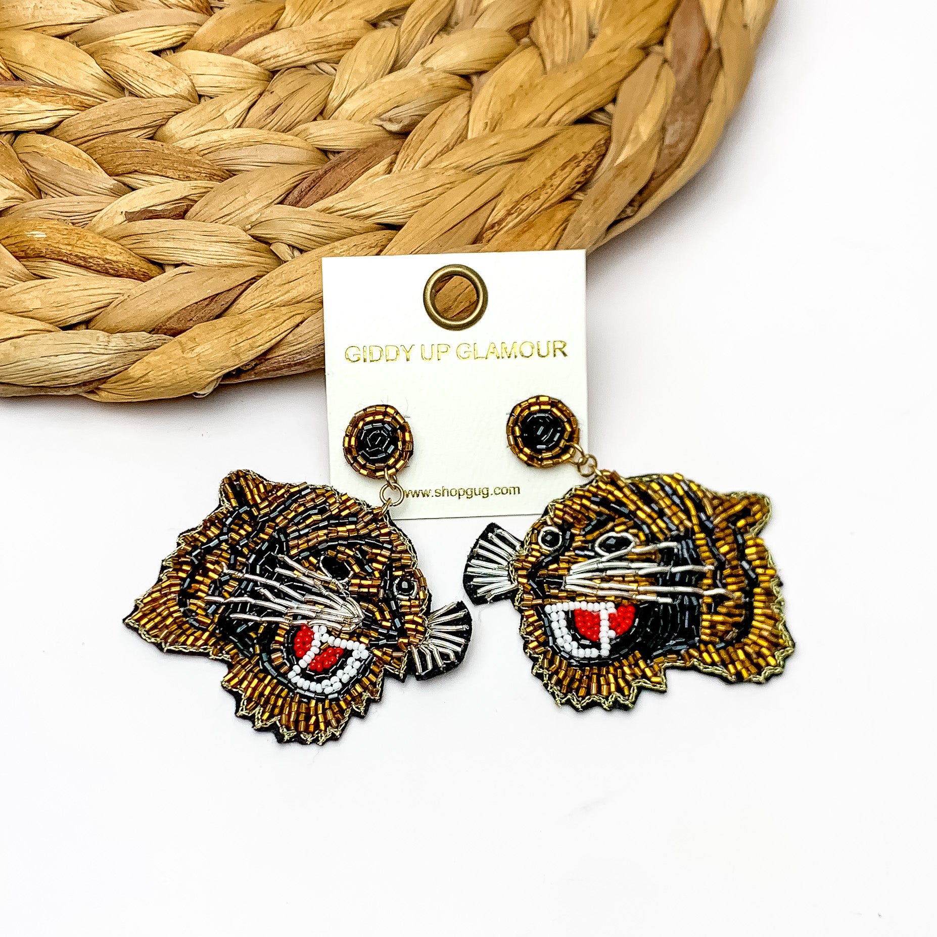 Tiger Beaded Drop Earrings in Gold and Black. The earrings are laying against a woven piece. The background of the picture is white.