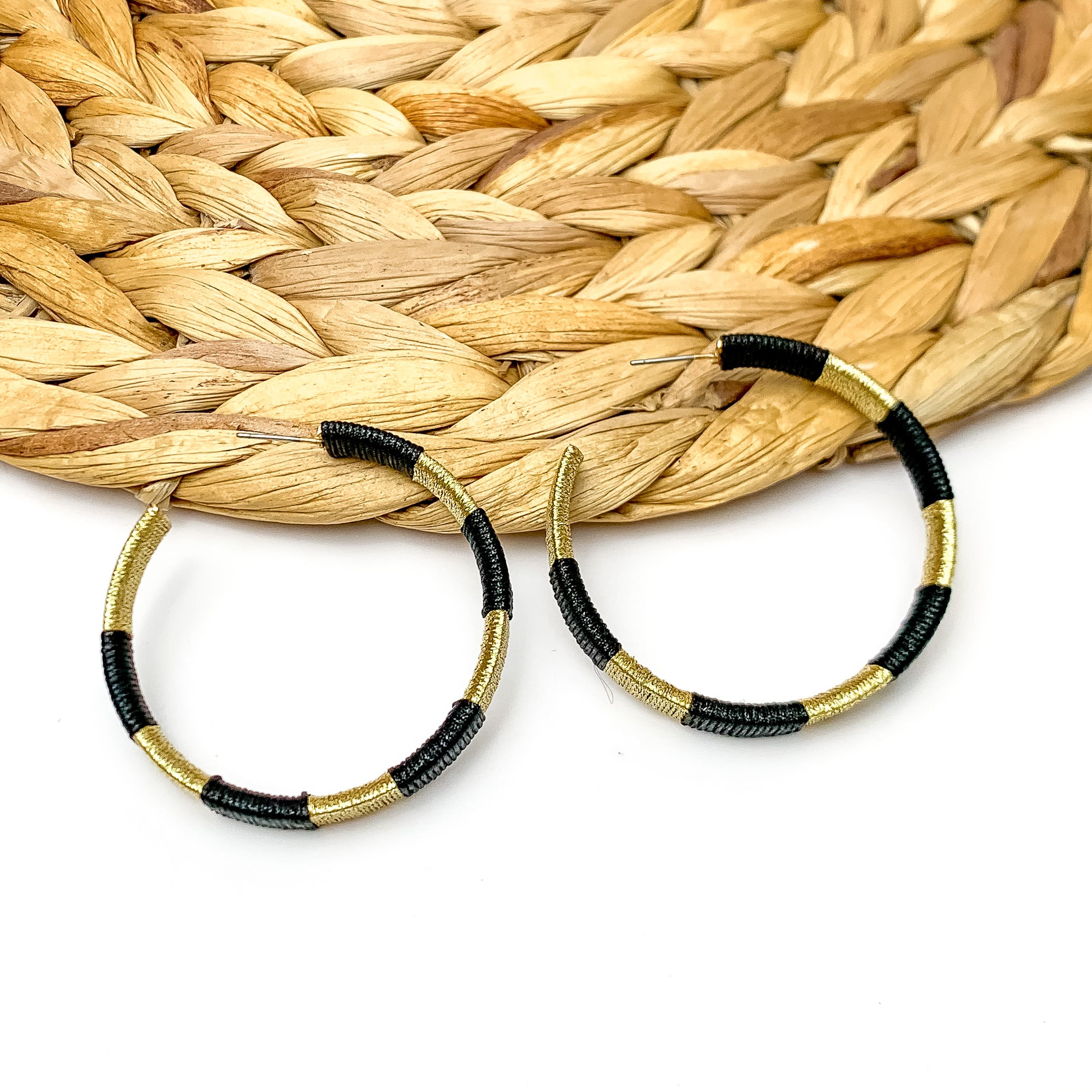 Game Day Glam Colored Hoop Earrings in Black and Gold. The two colored hoops are laying against a woven decoration with a white background.