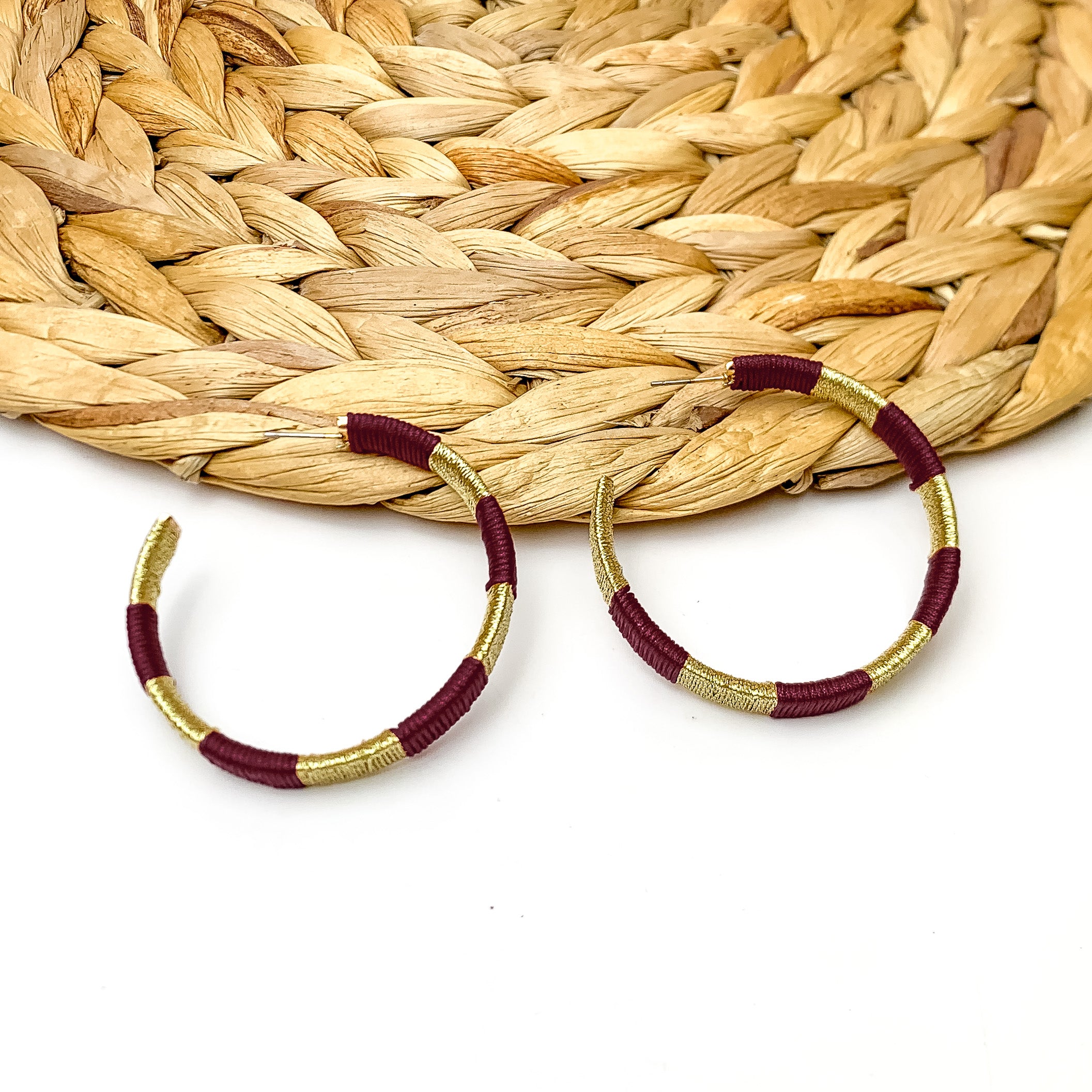 Game Day Glam Colored Hoop Earrings in Maroon and Gold. The two colored hoops are laying against a woven decoration with a white background.