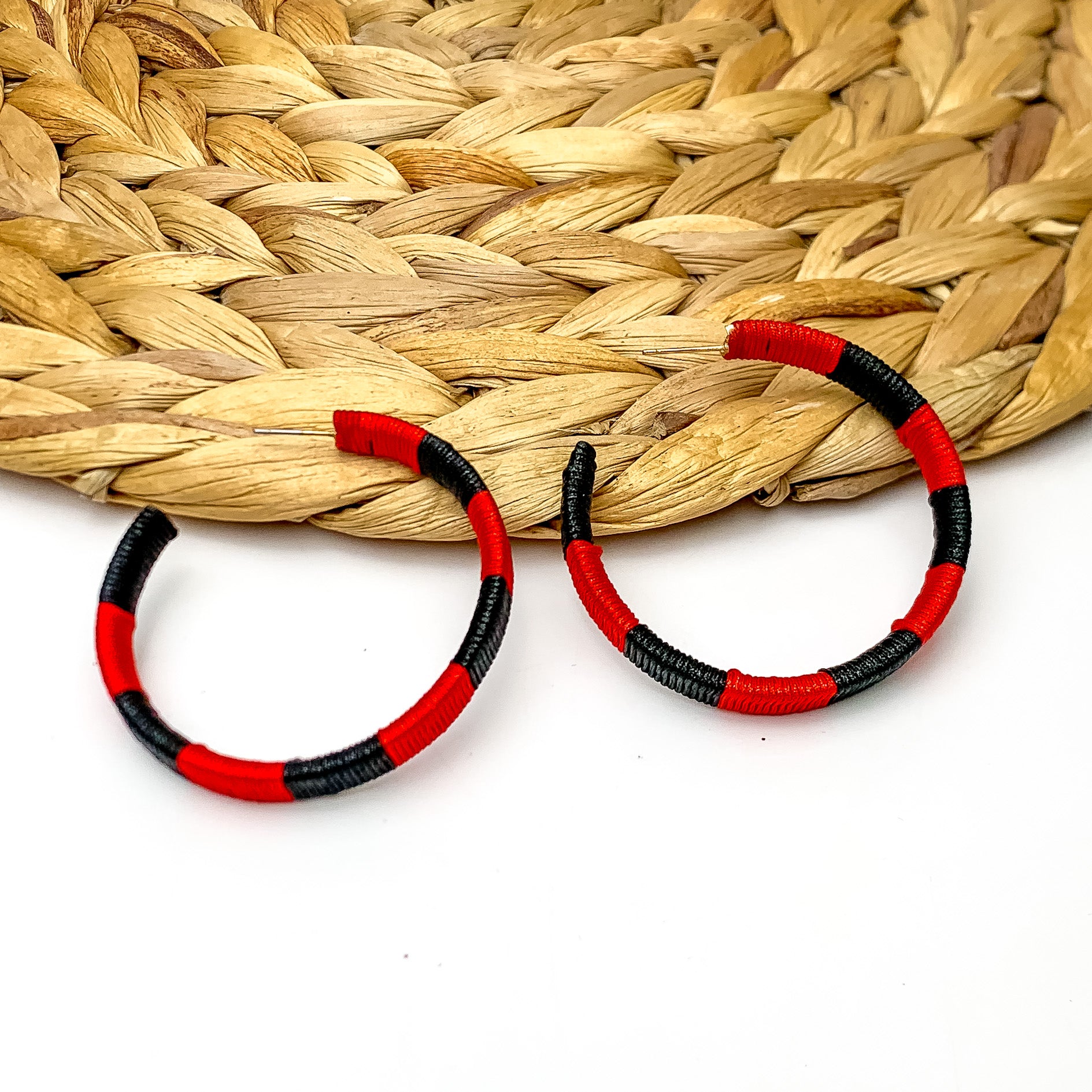 Game Day Glam Colored Hoop Earrings in Black and Red. The two colored hoops are laying against a woven decoration with a white background.