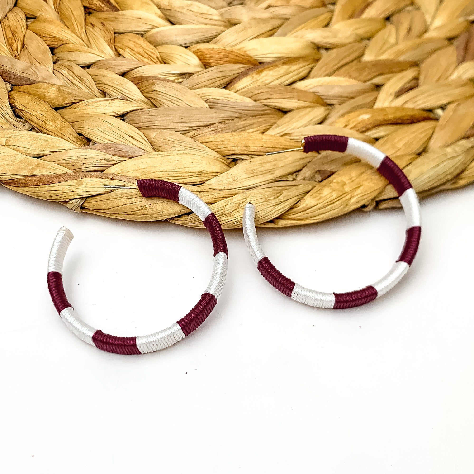 Game Day Glam Colored Hoop Earrings in Maroon and White. The two colored hoops are laying against a woven decoration with a white background.