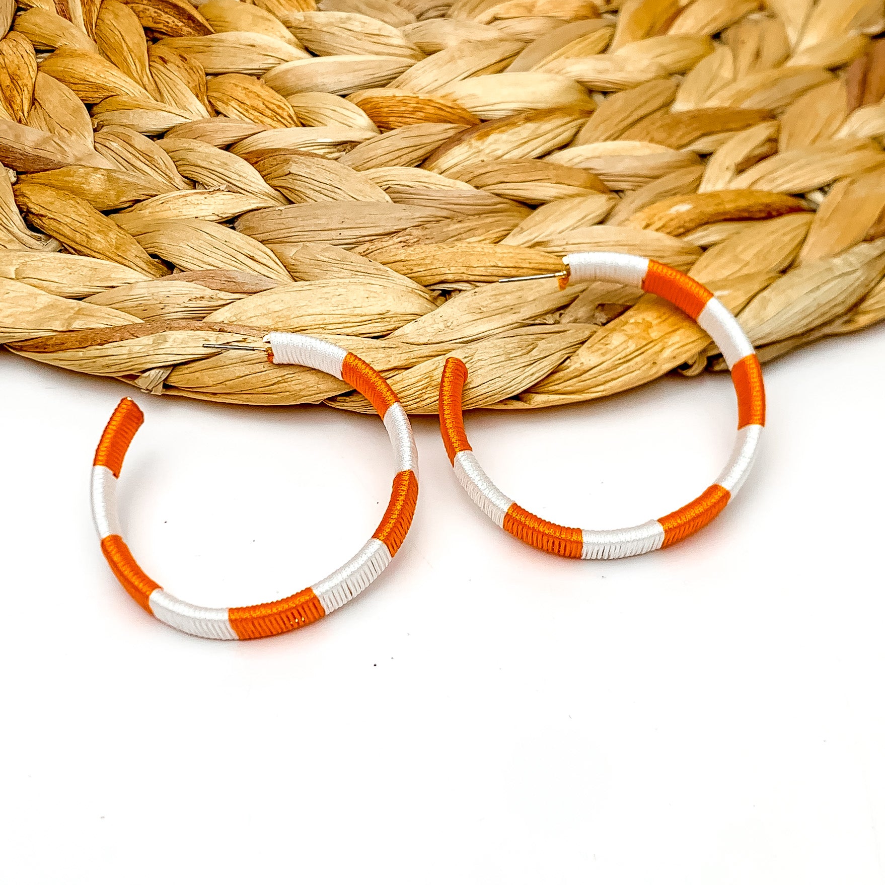 Game Day Glam Colored Hoop Earrings in Orange and White. The two colored hoops are laying against a woven decoration with a white background.