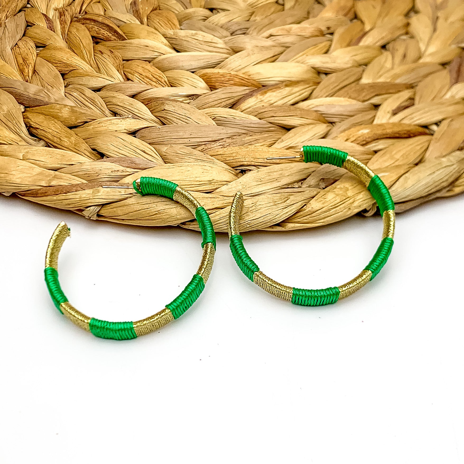 Game Day Glam Colored Hoop Earrings in Green and Gold. The two colored hoops are laying against a woven decoration with a white background.